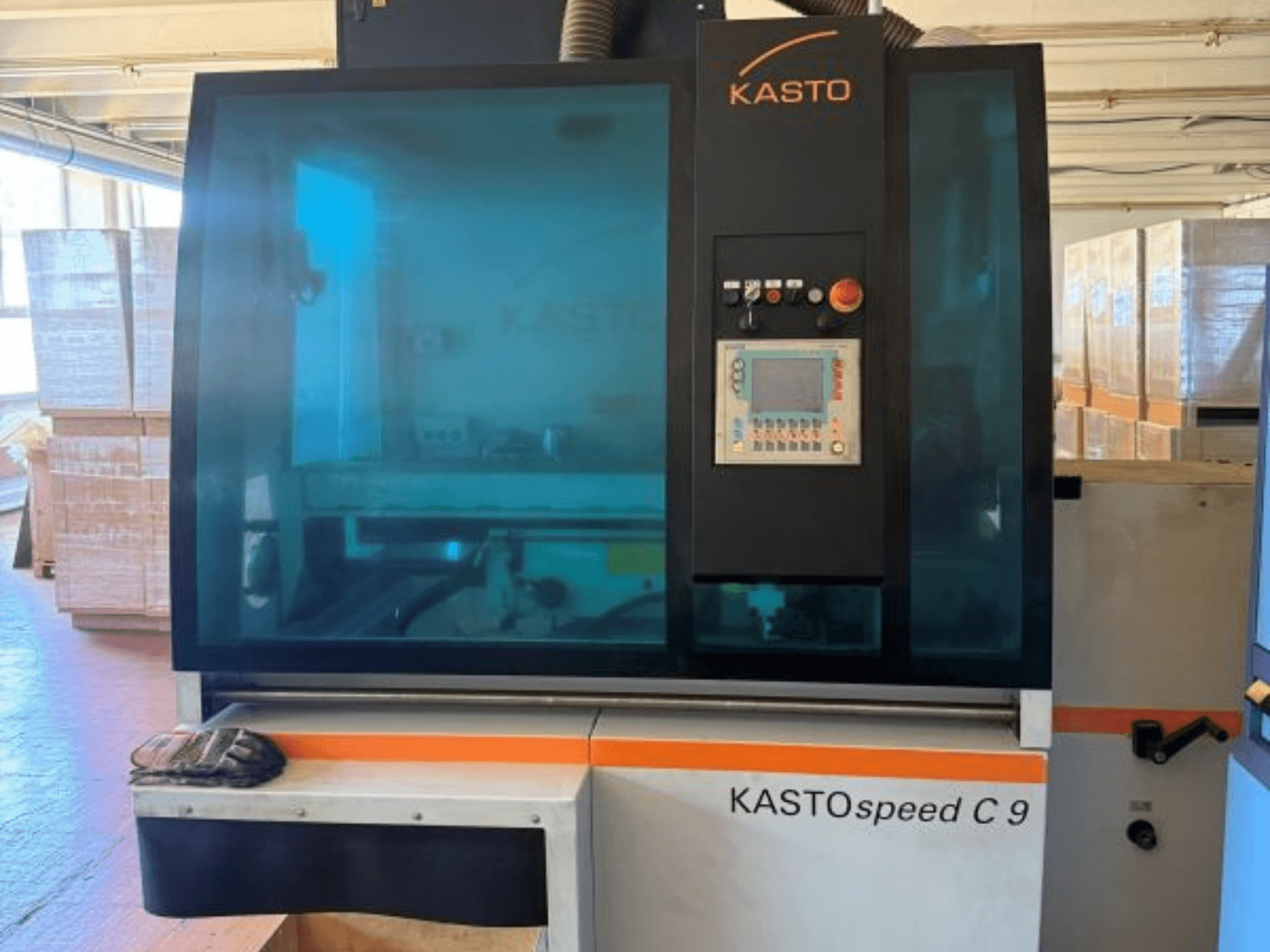Framifrånvy av cirkelsågen KASTO KASTOspeed C 9, med kontrollpanel och säkerhetsglas, med trälådor i bakgrunden.