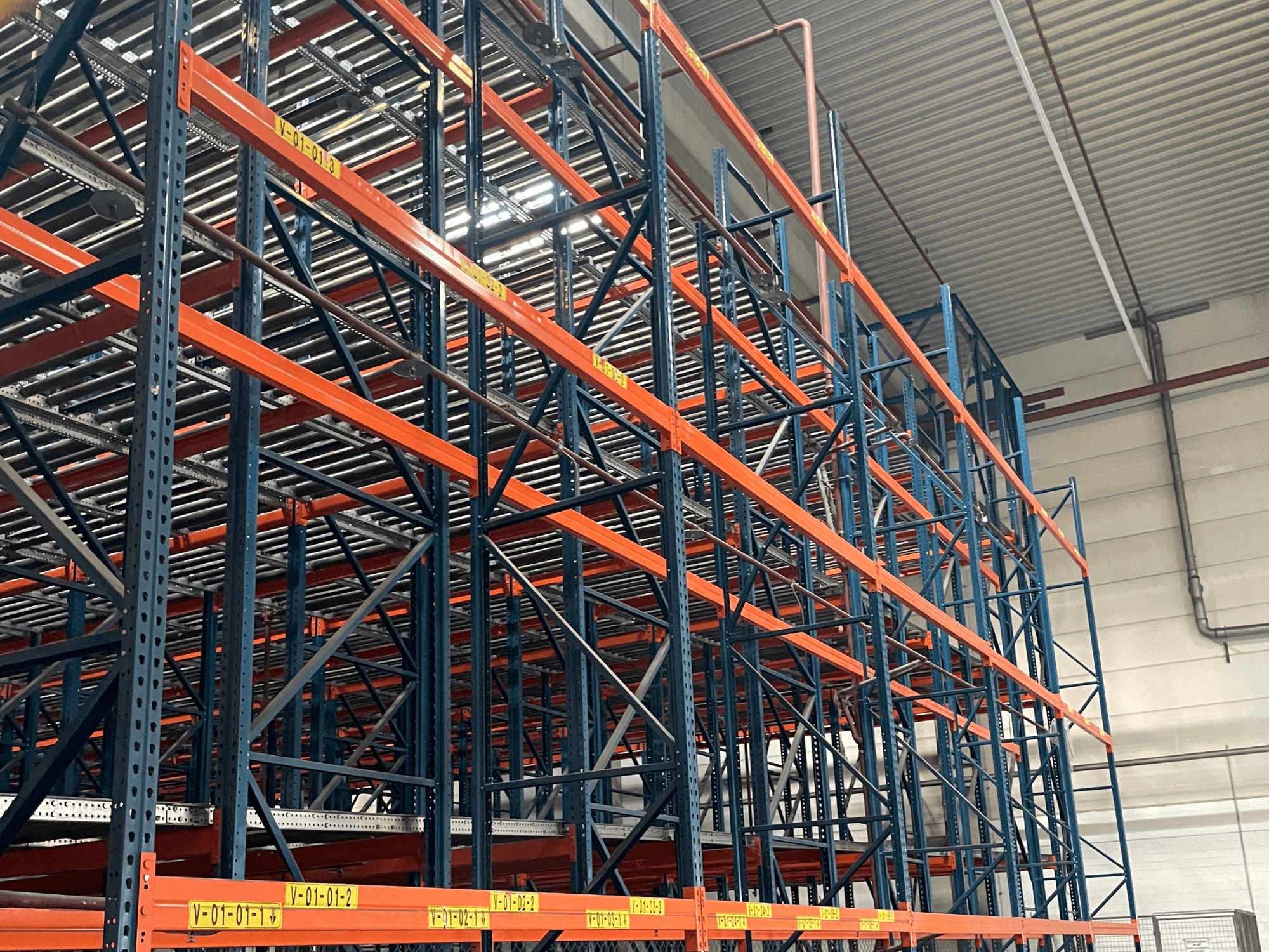 FL SYSTEME F05.10 FLG pallhanteringssystem i en lagerlokal, sett från sidan, med kraftiga orange och blå ställningar.