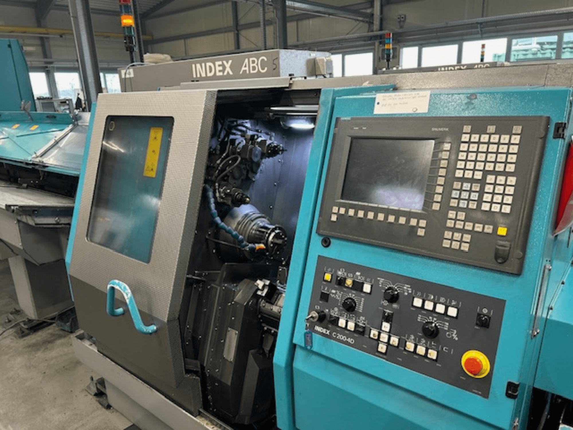 Frontvy av en INDEX C200-AD CNC-svarv med kontrollpanel, synliga interna komponenter och säkerhetsanordningar.