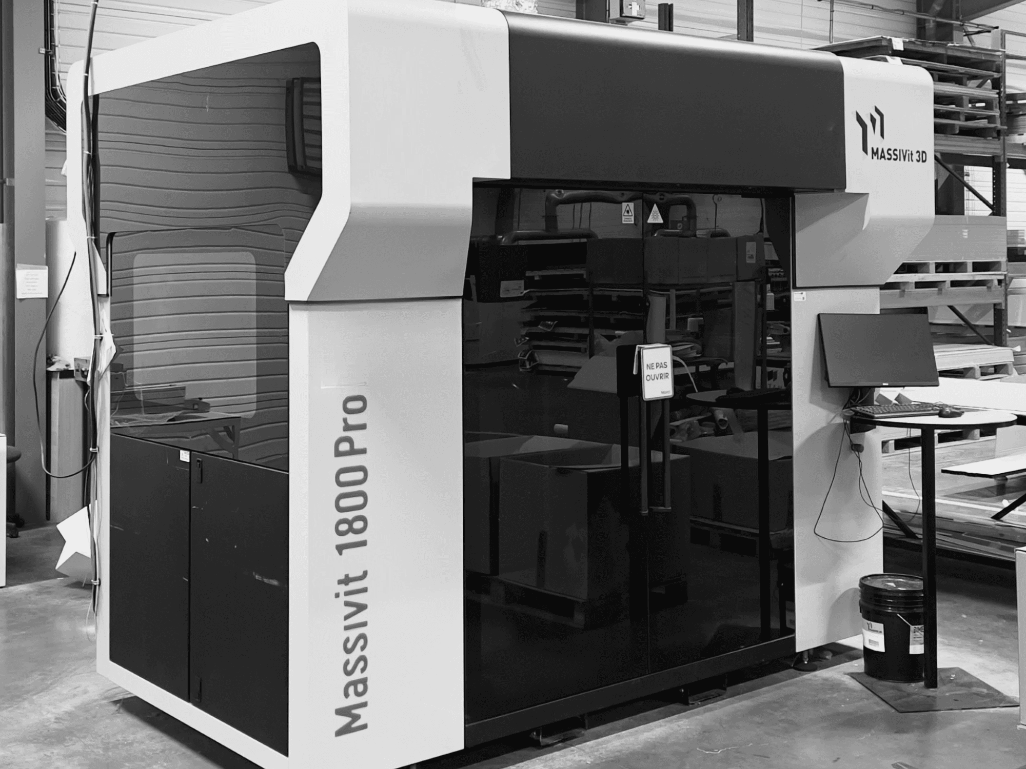 3D-skrivaren MASSIVIT 1800 PRO i en verkstad, sett framifrån, med en datorarbetsstation och en kontrollpanel synliga.