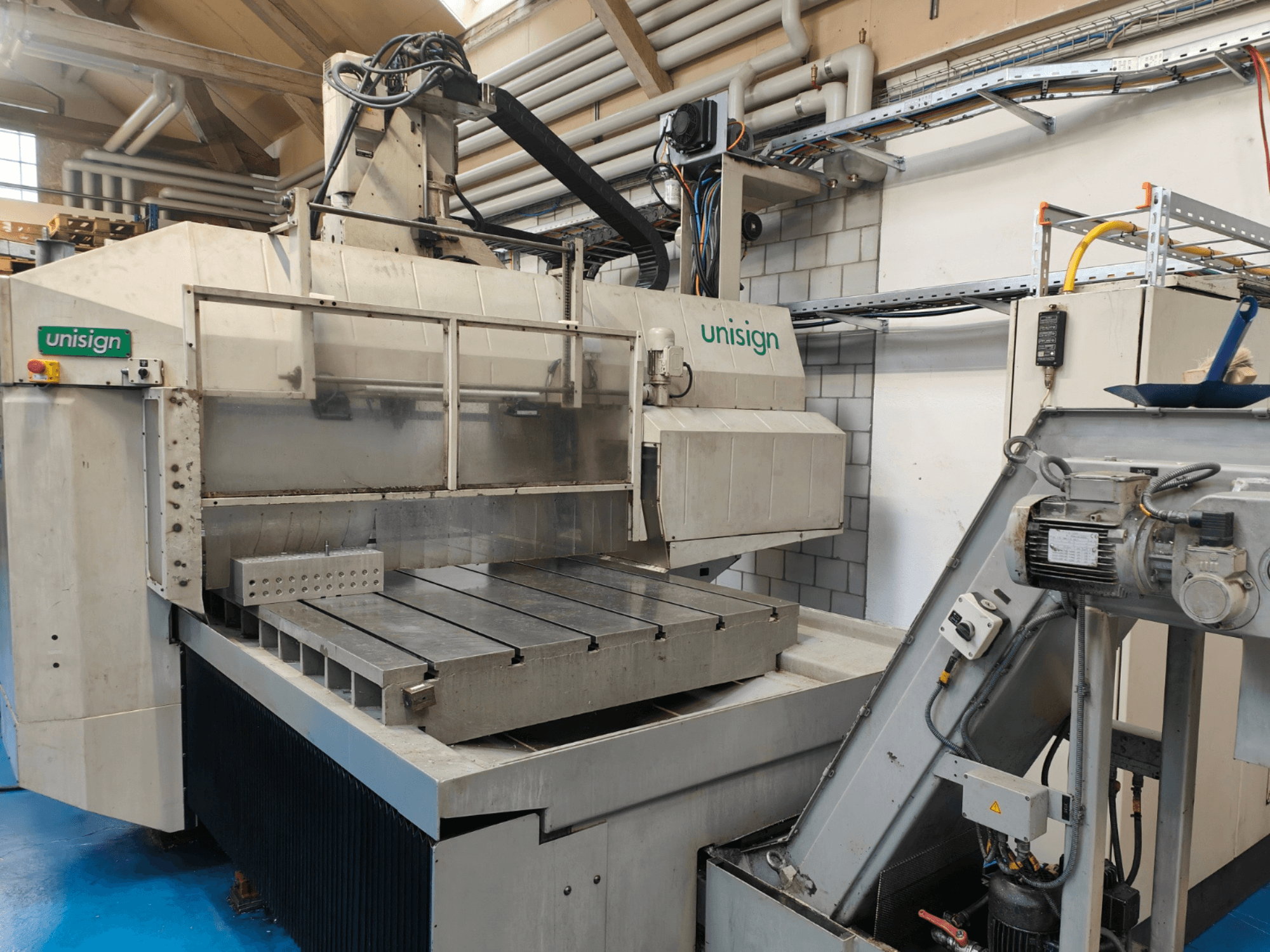 Unisign CNC-maskin i en verkstad, vy framifrån, med ett stort bord, kontrollpanel och industriella designelement.