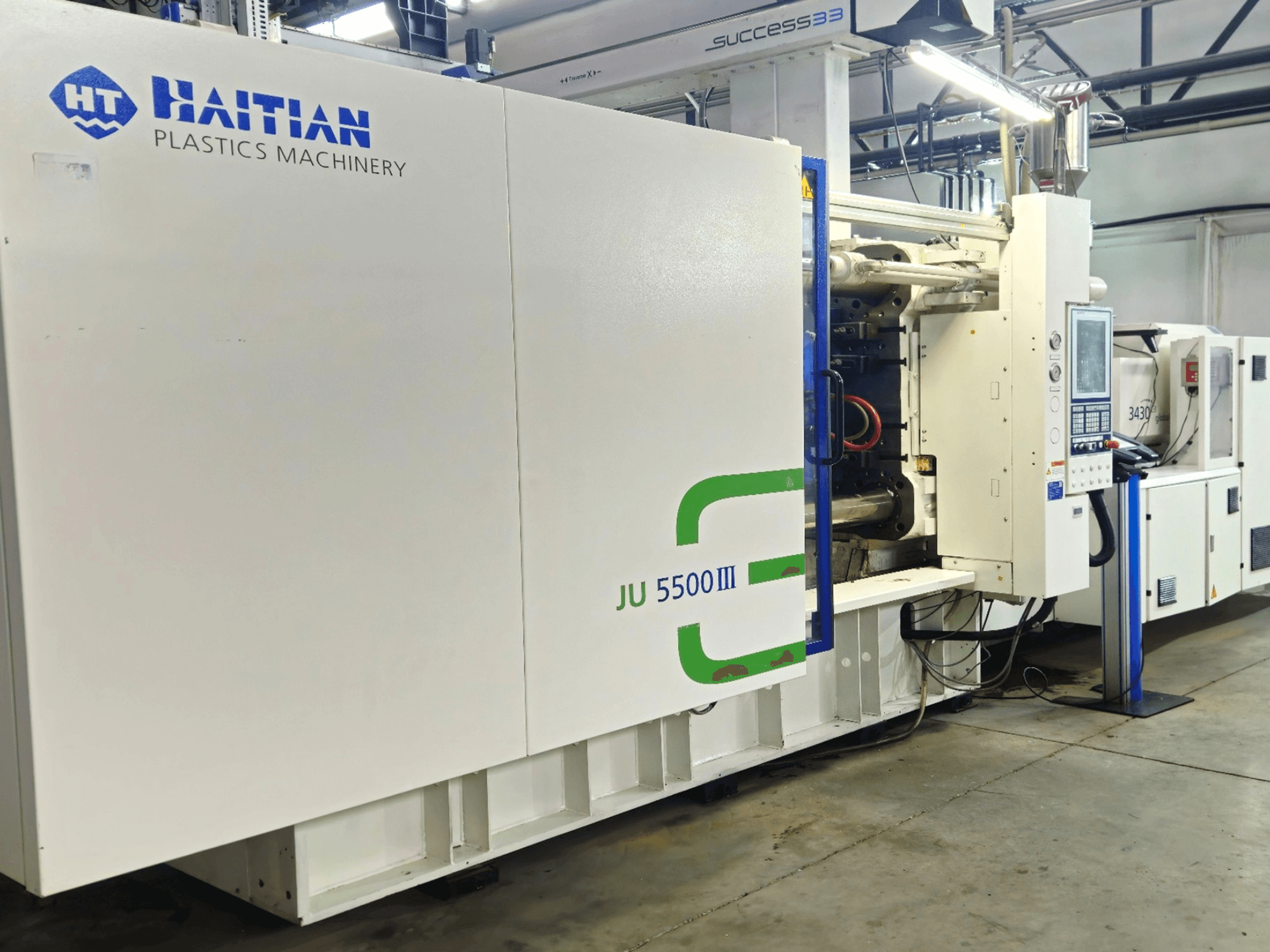 Haitisk JU 5500III plastmaskin i fabriksmiljö, frontvy som visar kontrollpanel och produktionsområde.