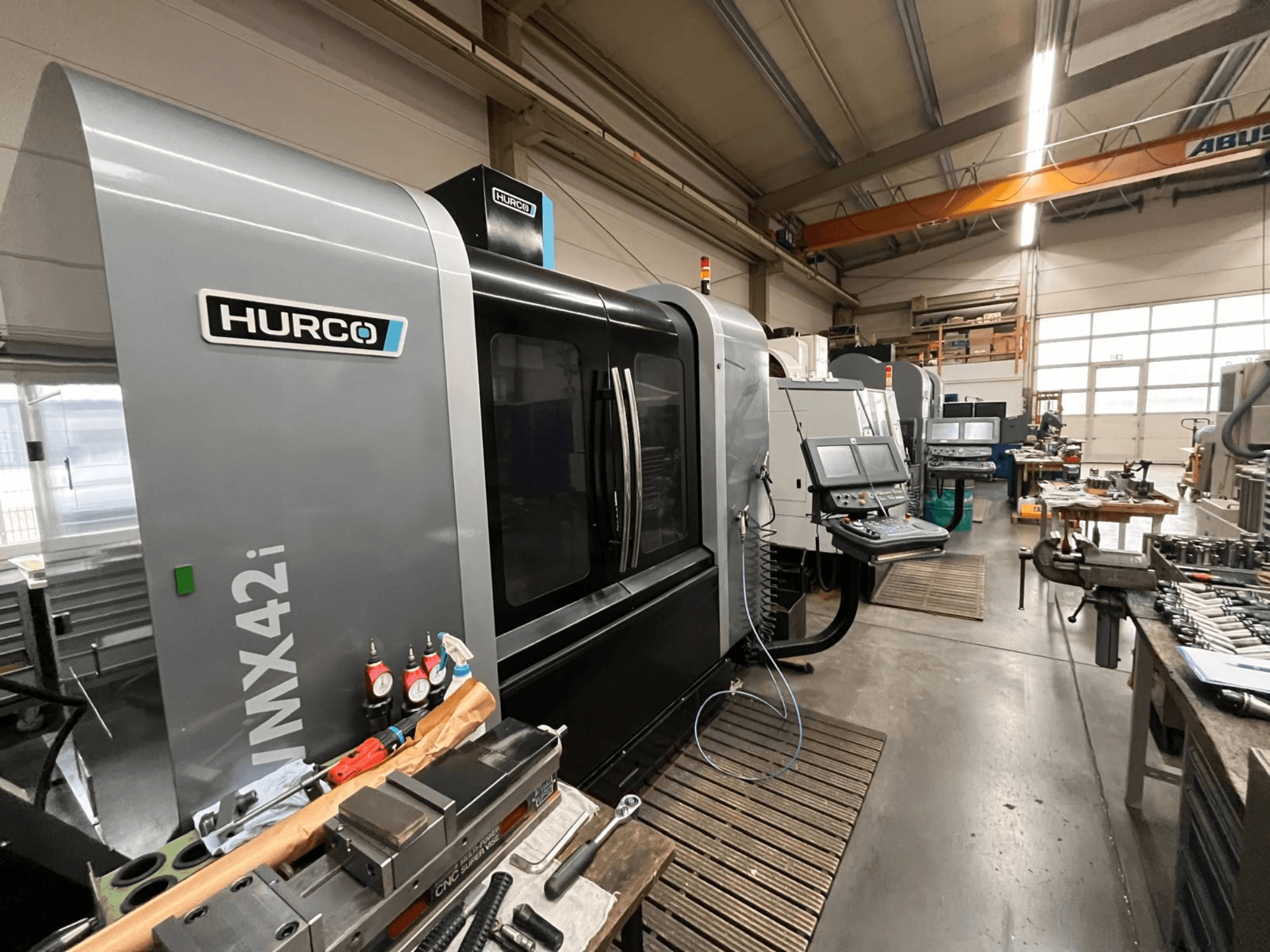 Hurco VMX42i CNC-maskin i verkstad, vy framifrån. Med kontrollpanel, grå kaross och industriell omgivning.