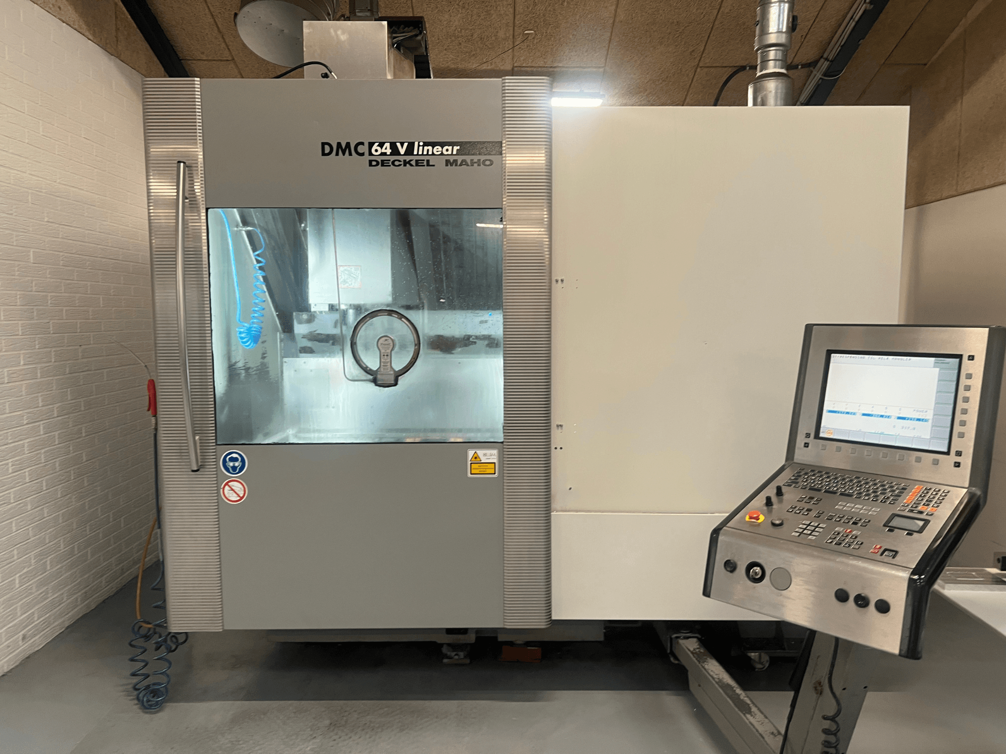 DMC 64 V Linear av Deckel Maho, CNC-bearbetningscenter sett framifrån med kontrollpanel och kylmedelsmunstycke synliga.