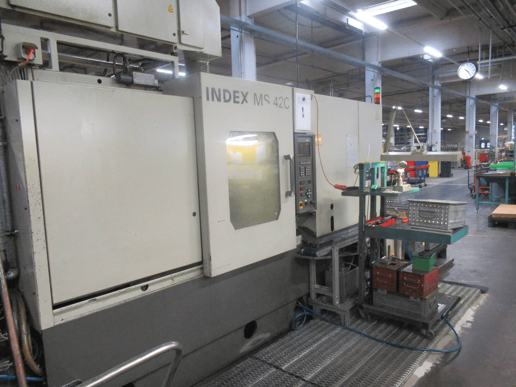 INDEX MS 42C CNC-maskin i en verkstad, sidovy som visar kontrollpanel och verktygsförvaring på hjulförsedd vagn.