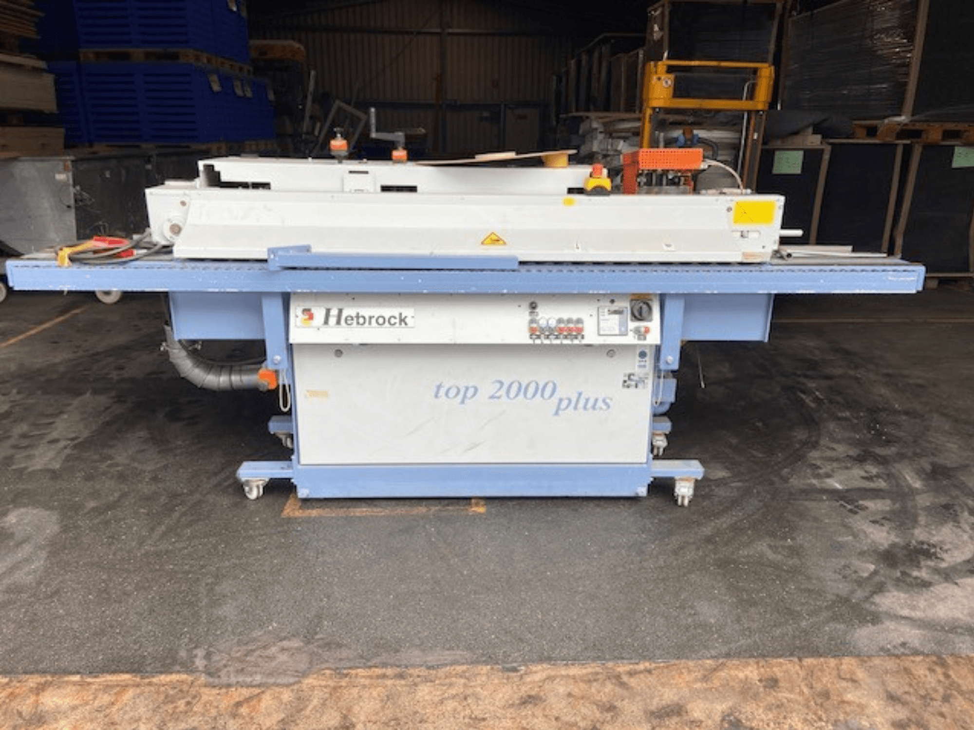 Hebrock Top 2000 Plus, framifrån; industriell elektrisk maskin med kontrollpanel, hjul för mobilitet och säkerhetsetiketter synliga.
