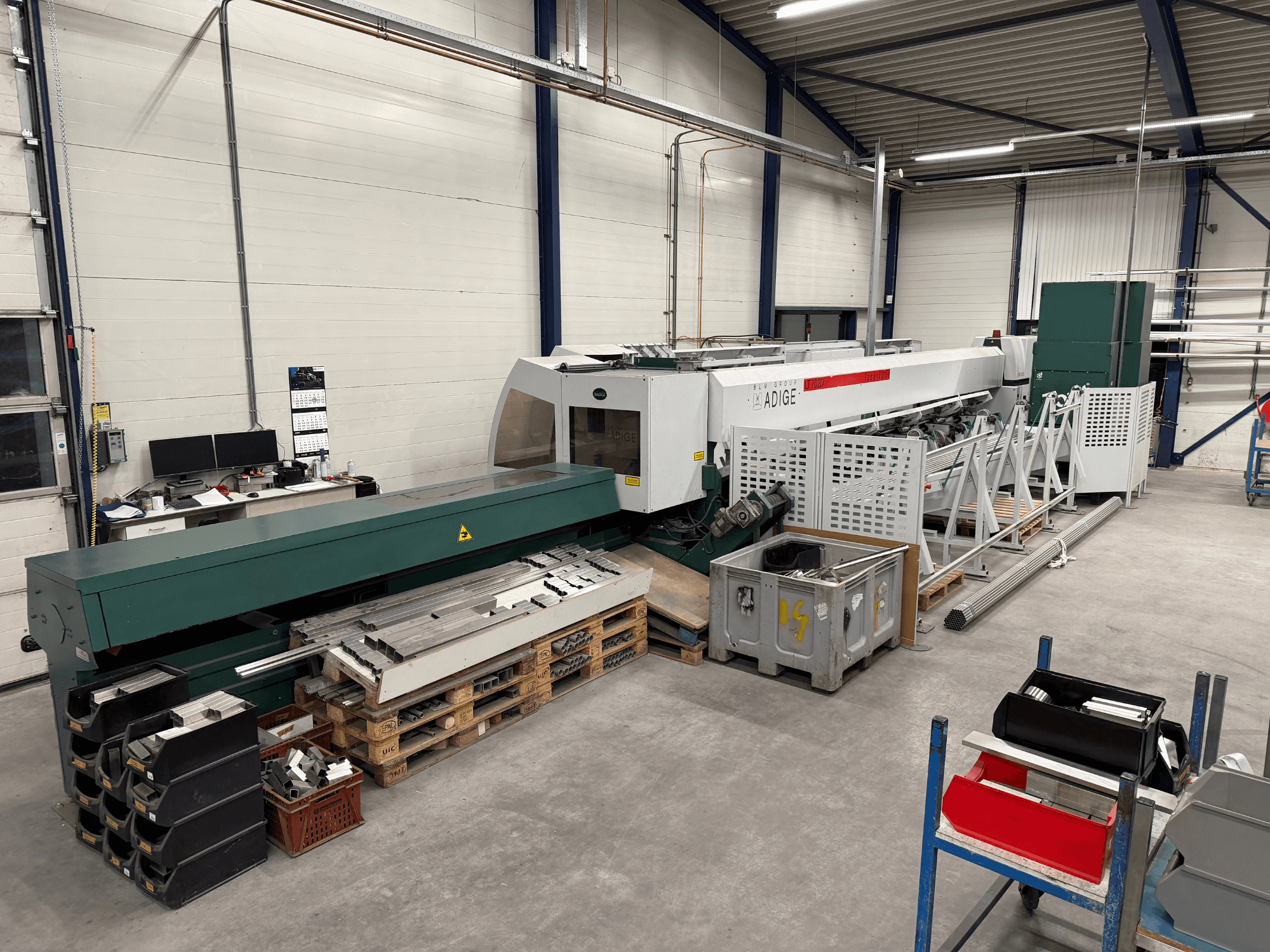 En BLM Adige LT702 CO₂-laserskärmaskin i en verkstad, sett från sidan, där metallkomponenter och röran på arbetsytan syns.