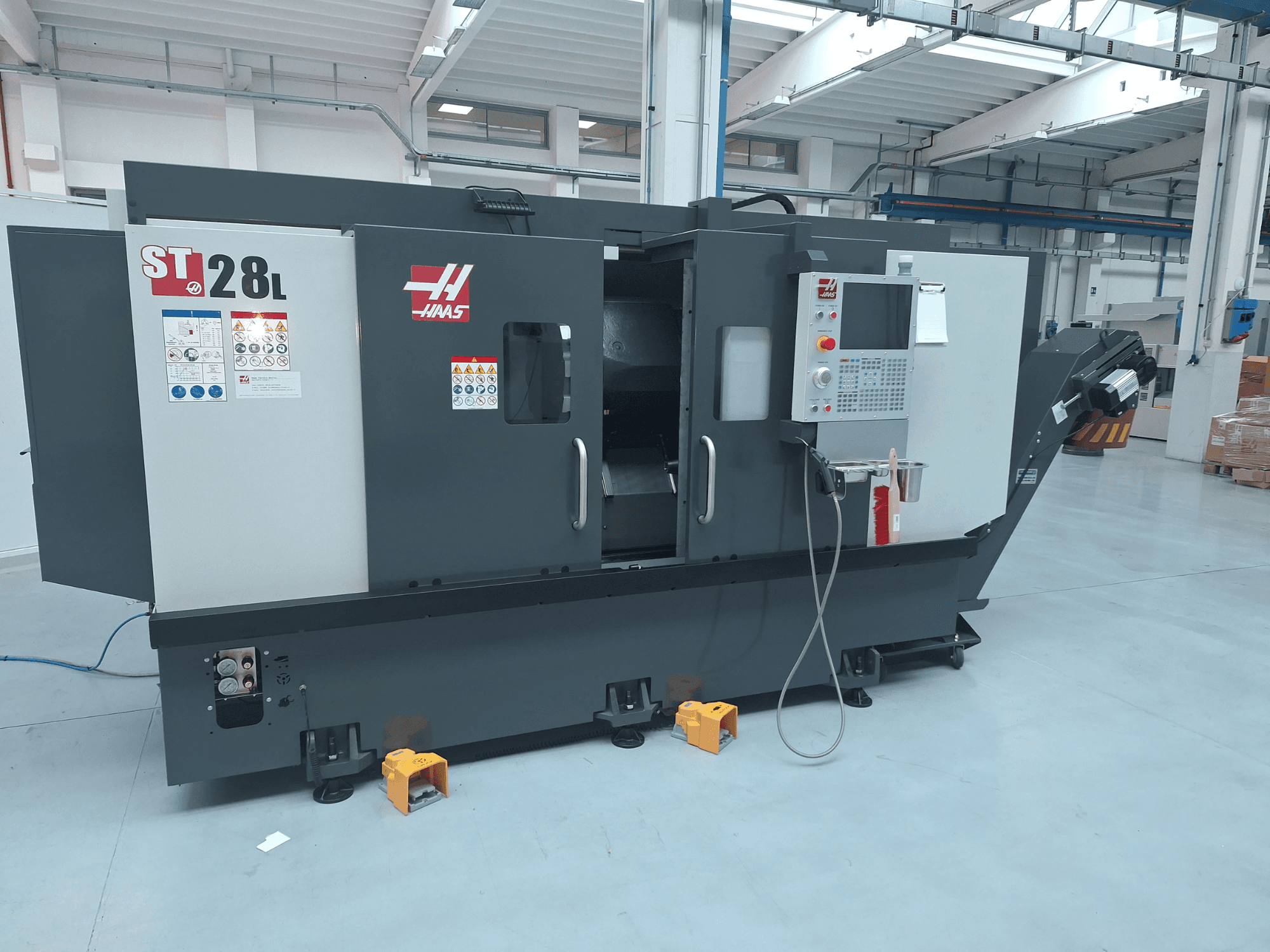 Sidovy av den horisontella svarven Haas ST-28L, med kontrollpanel, manöverknappar och säkerhetsmärkningar.