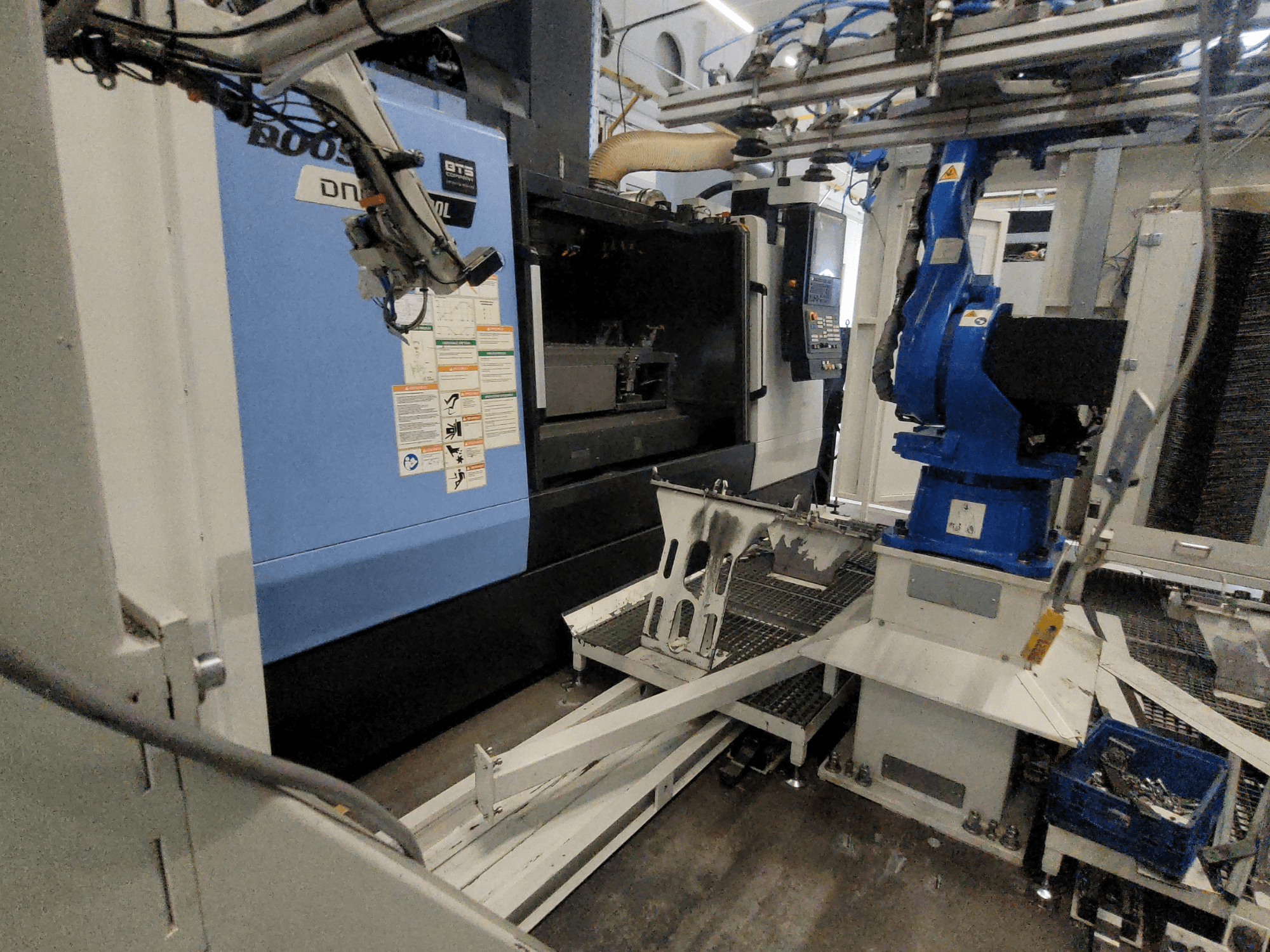 DOOSAN DNM 6700L vertikalt bearbetningscenter, sidovy, där robotarmen och kontrollpanelen syns, vilket visar maskinens uppställning.