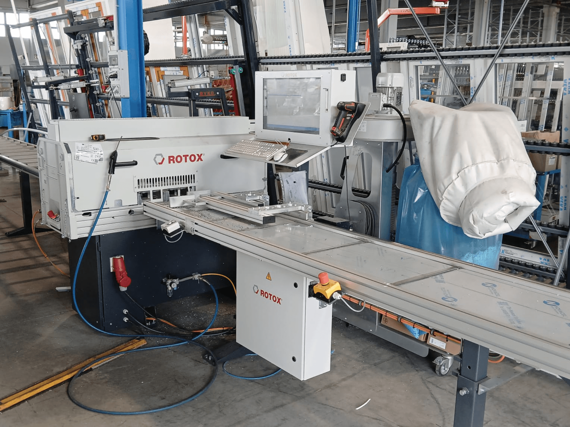Framifrånvy av en Rotox GLA401-plastbearbetningsmaskin med kontrollpanel, transportband och synliga slangar i en industriell miljö.