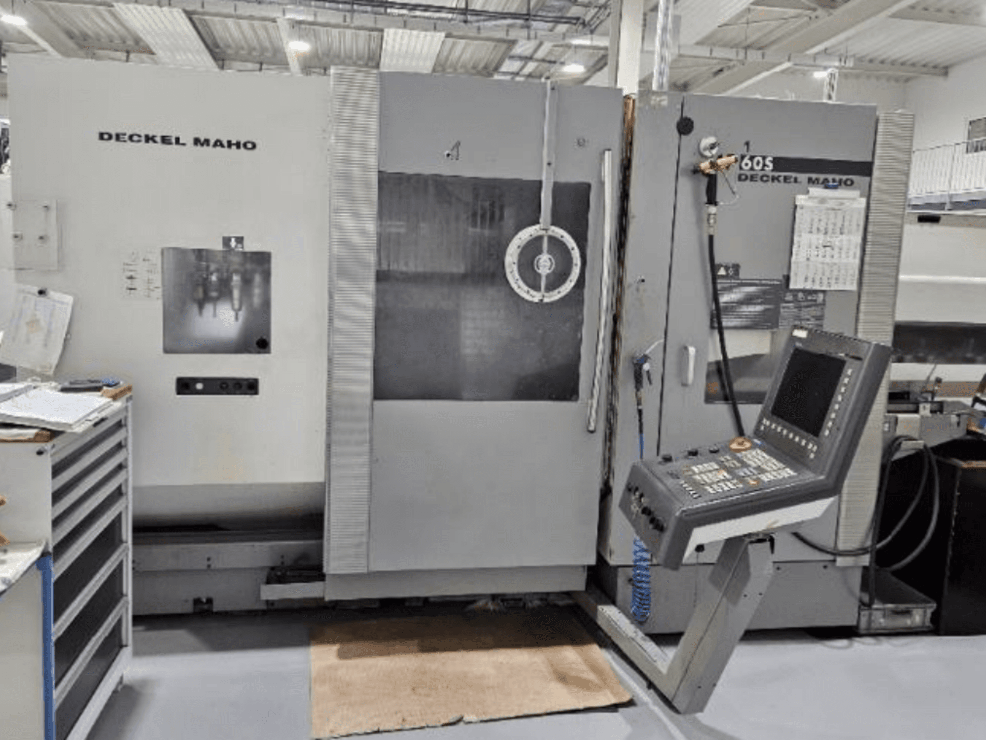 Frontvy av en DECKEL MAHO 60S CNC-maskin med kontrollpanel och synliga verktyg, i en verkstadsmiljö.