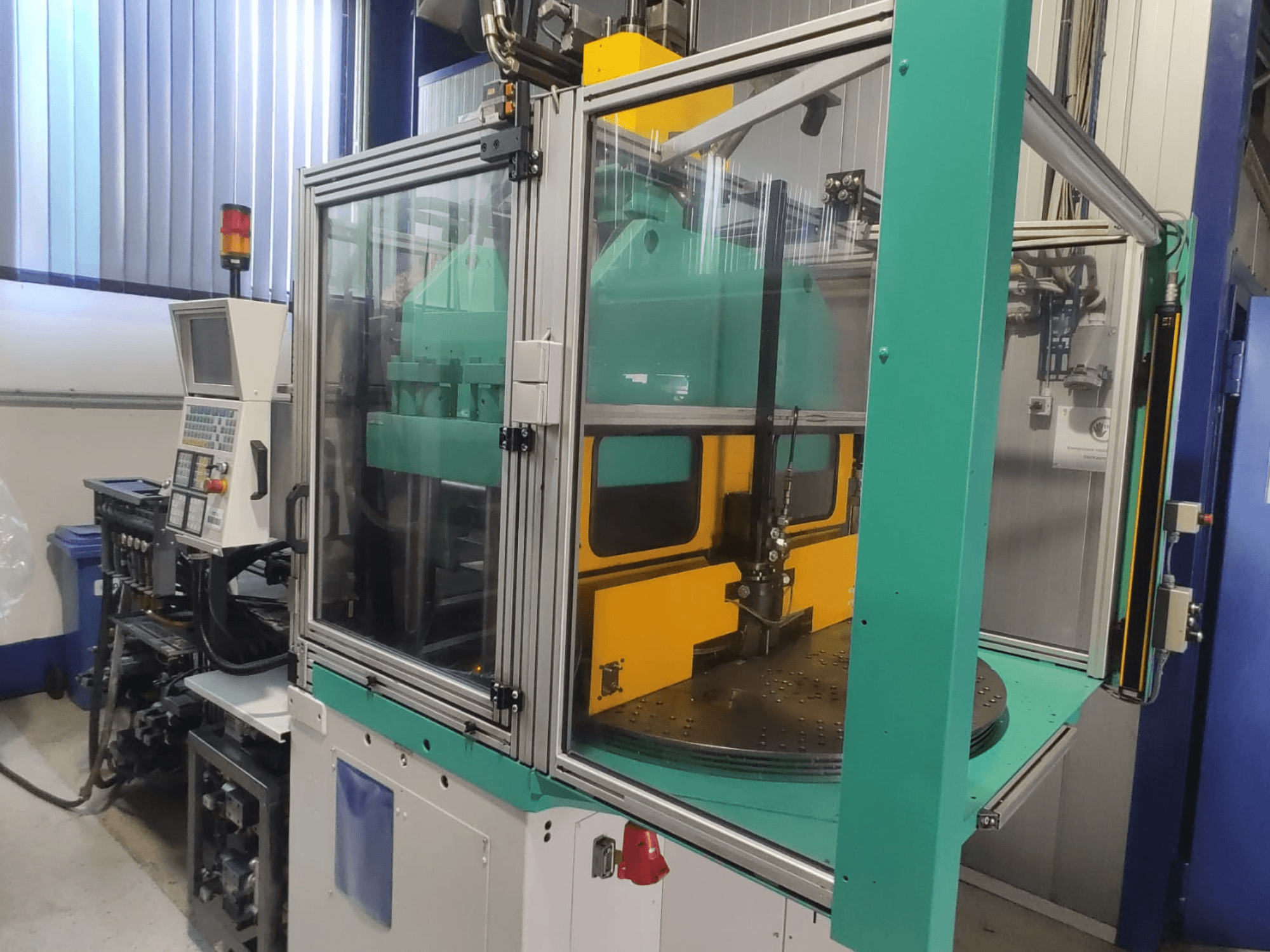 Arburg 1200 TS 800-60-350 vertikal formsprutningsmaskin, framifrån med kontrollpanelen och skyddshöljet i förgrunden.