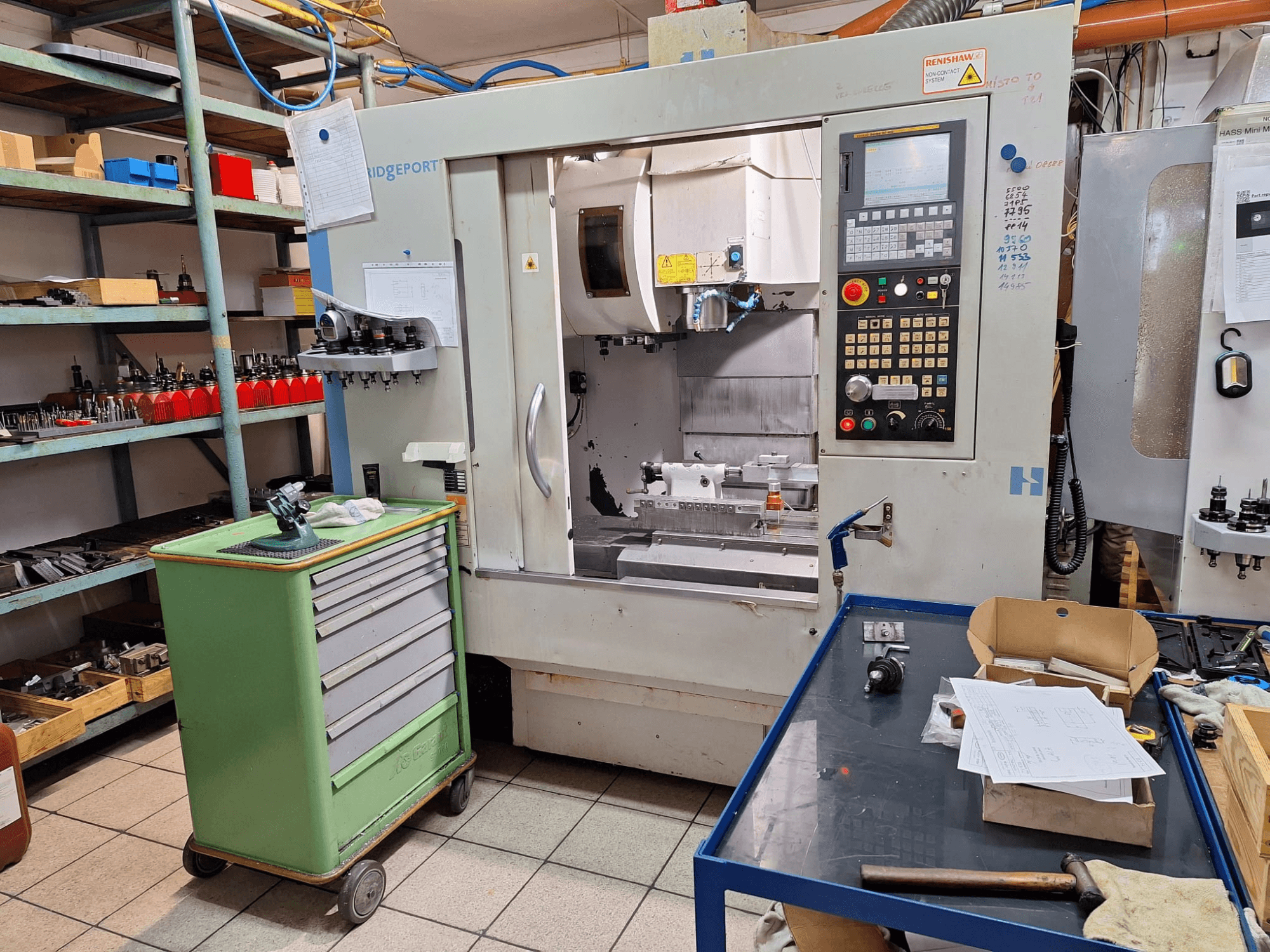 Framifrån sett på det vertikala bearbetningscentret Hardinge Bridgeport GX 710 med kontrollpanel, verktyg och hyllor i en verkstadsmiljö.