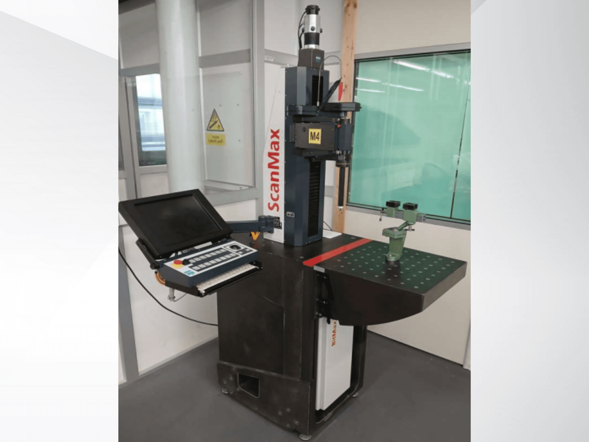 ScanMax M4 mätmaskin, framifrån med kontrollpanel och grön kalibreringsfixtur på ett streckat arbetsbord.