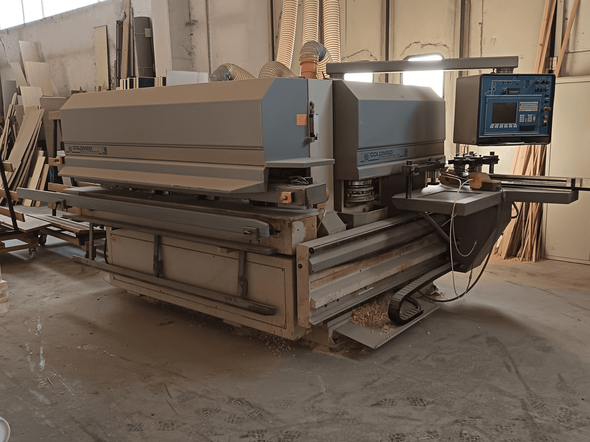 Colombo träbearbetningsmaskin, sidovy, visar kontrollpanelen, kapskivor och ansamling av sågspån i verkstaden.