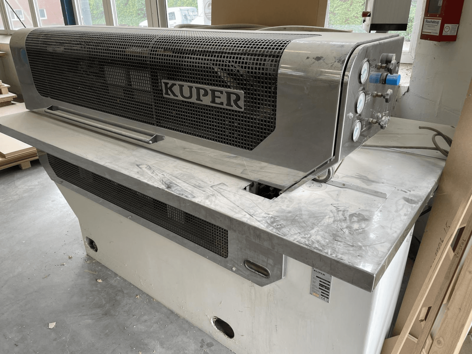 Fanérgiljotin KUPER FLI, framifrån, med stomme i rostfritt stål, mätinstrument och ett rent skärområde på en arbetsbänk.