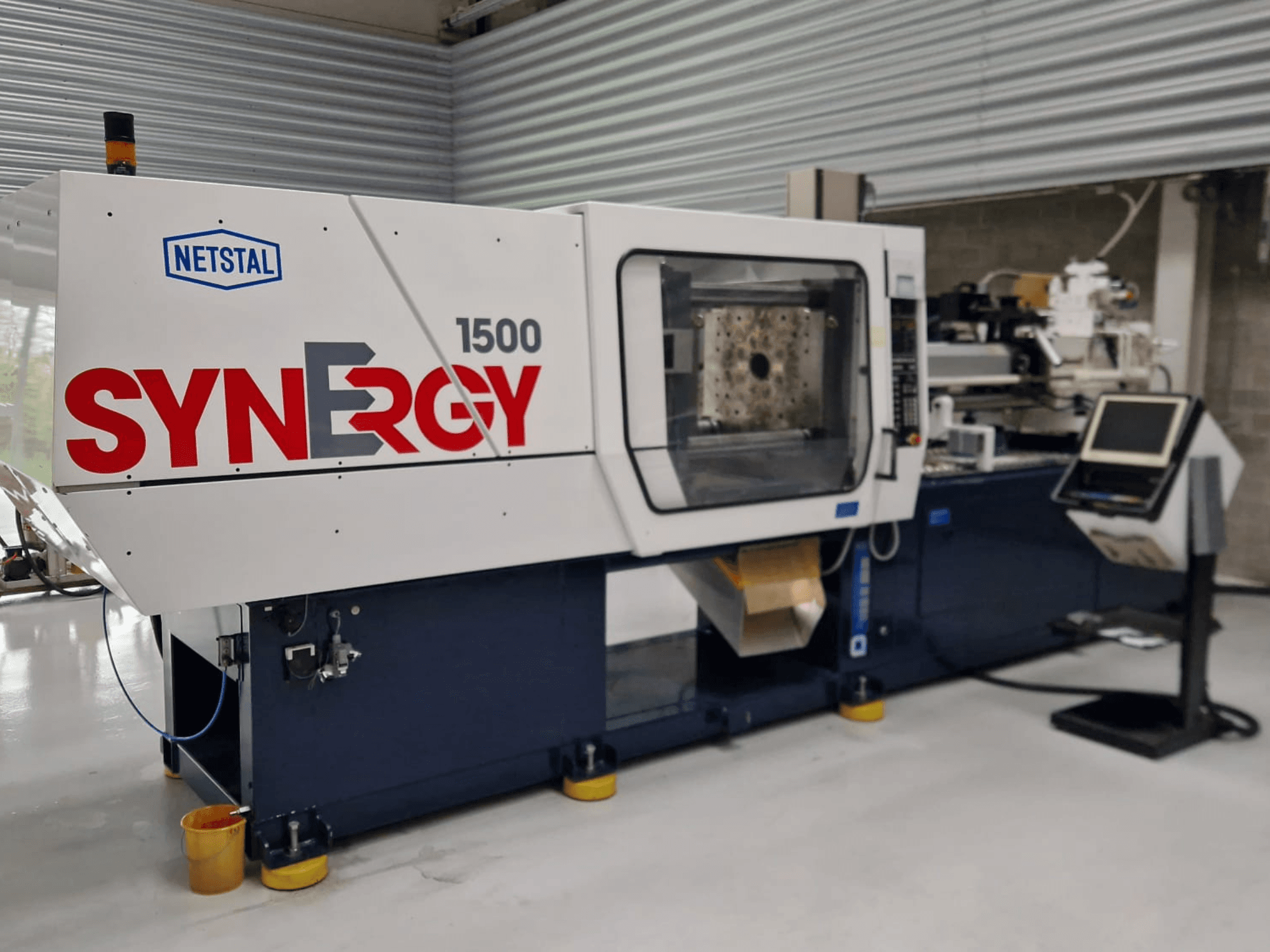 Netstal Synergy 1500-460 hydraulisk formsprutningsmaskin, framifrån, visar kontrollpanelen och det öppna formsprutningsområdet.