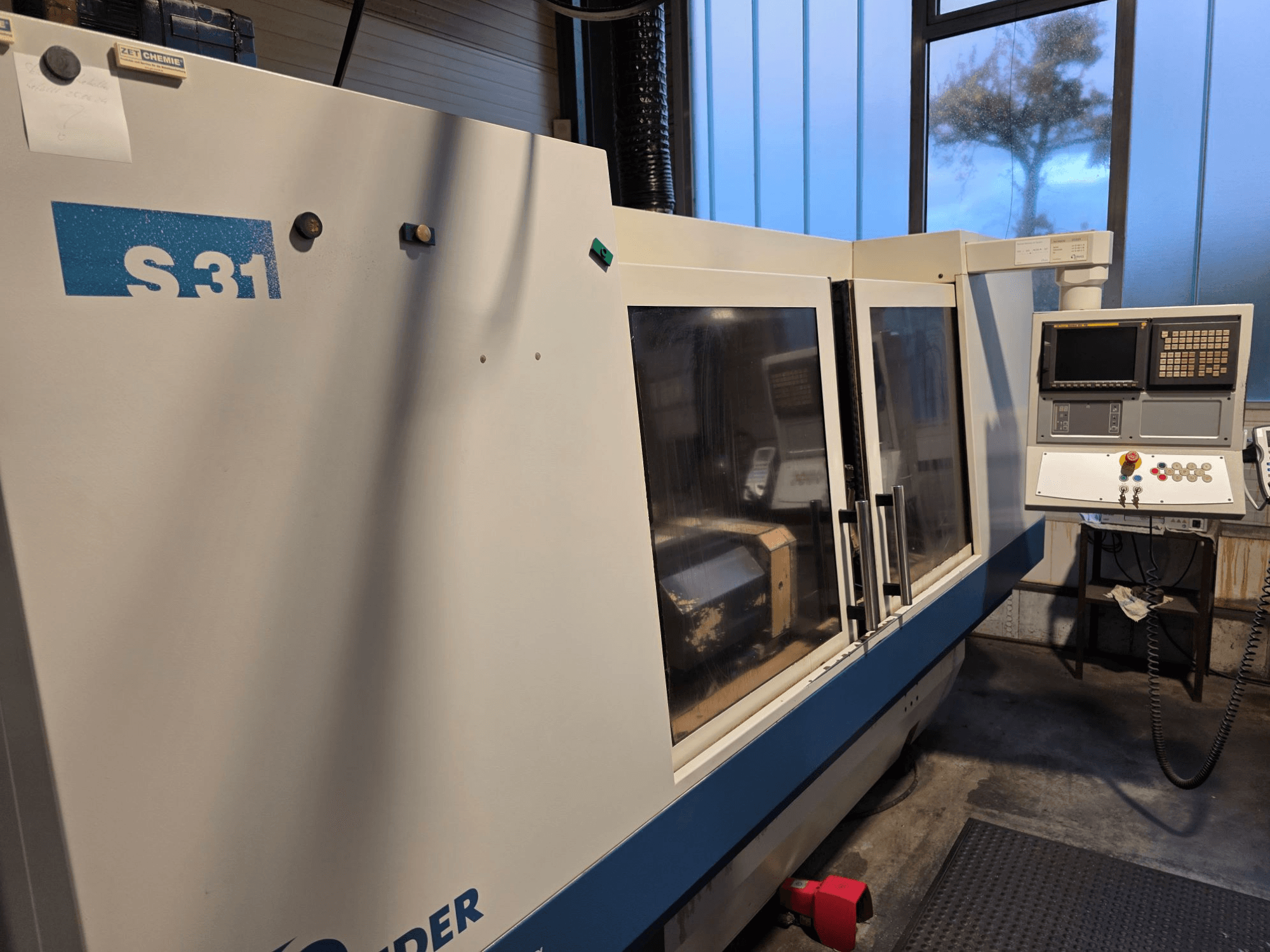 S31 CNC-slipmaskin, vy framifrån, har kontrollpanel med skärm och knappar, stor glasdörr, industriell miljö.