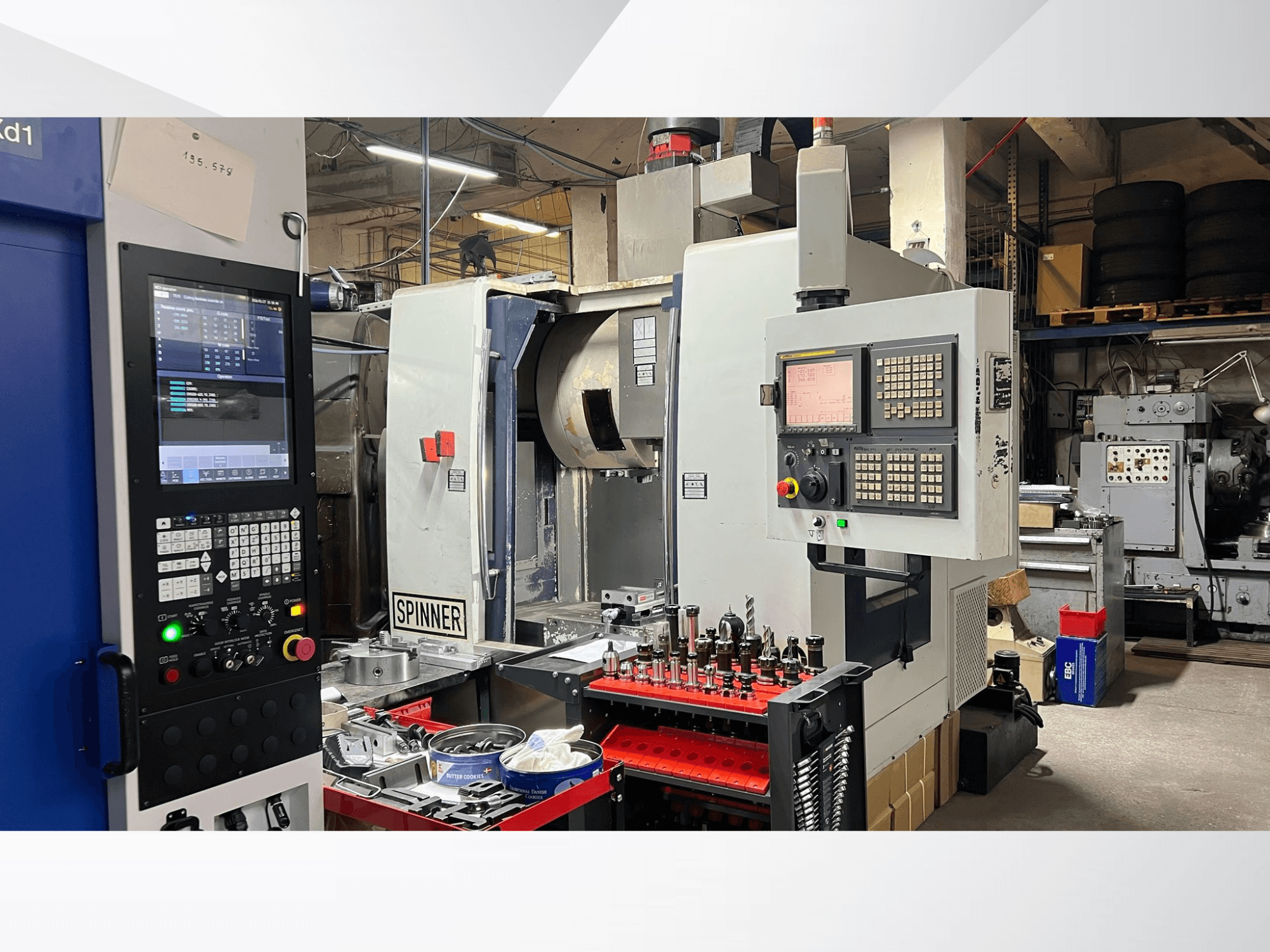 CNC-maskin med kontrollpanel, verktyg och arbetsstycken synliga, sedd framifrån i en verkstadsmiljö.