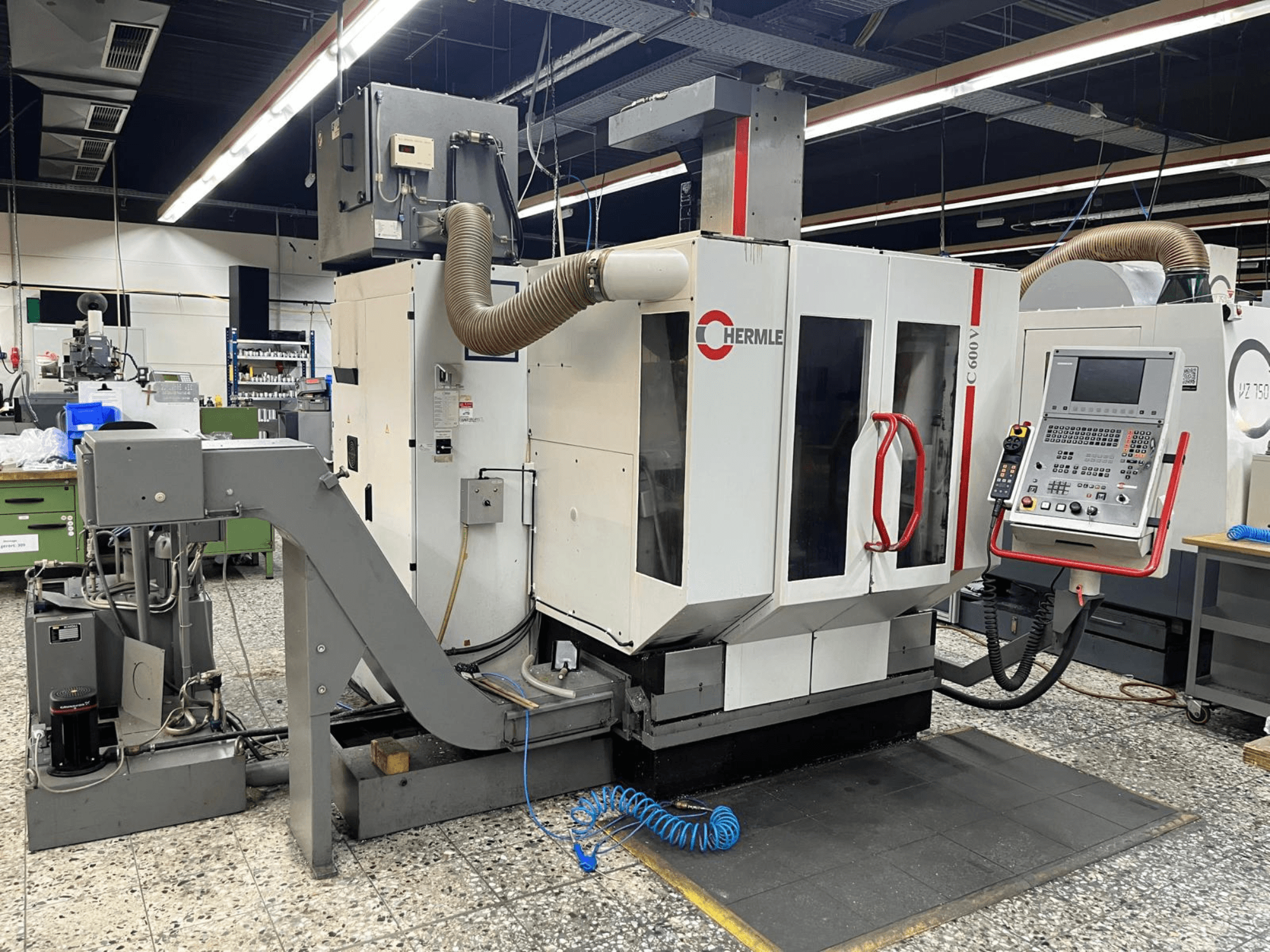 HERMLE C 600 V vertikal fleroperationsmaskin i en verkstad, framifrån med kontrollpanel och ventilationsanordningar.