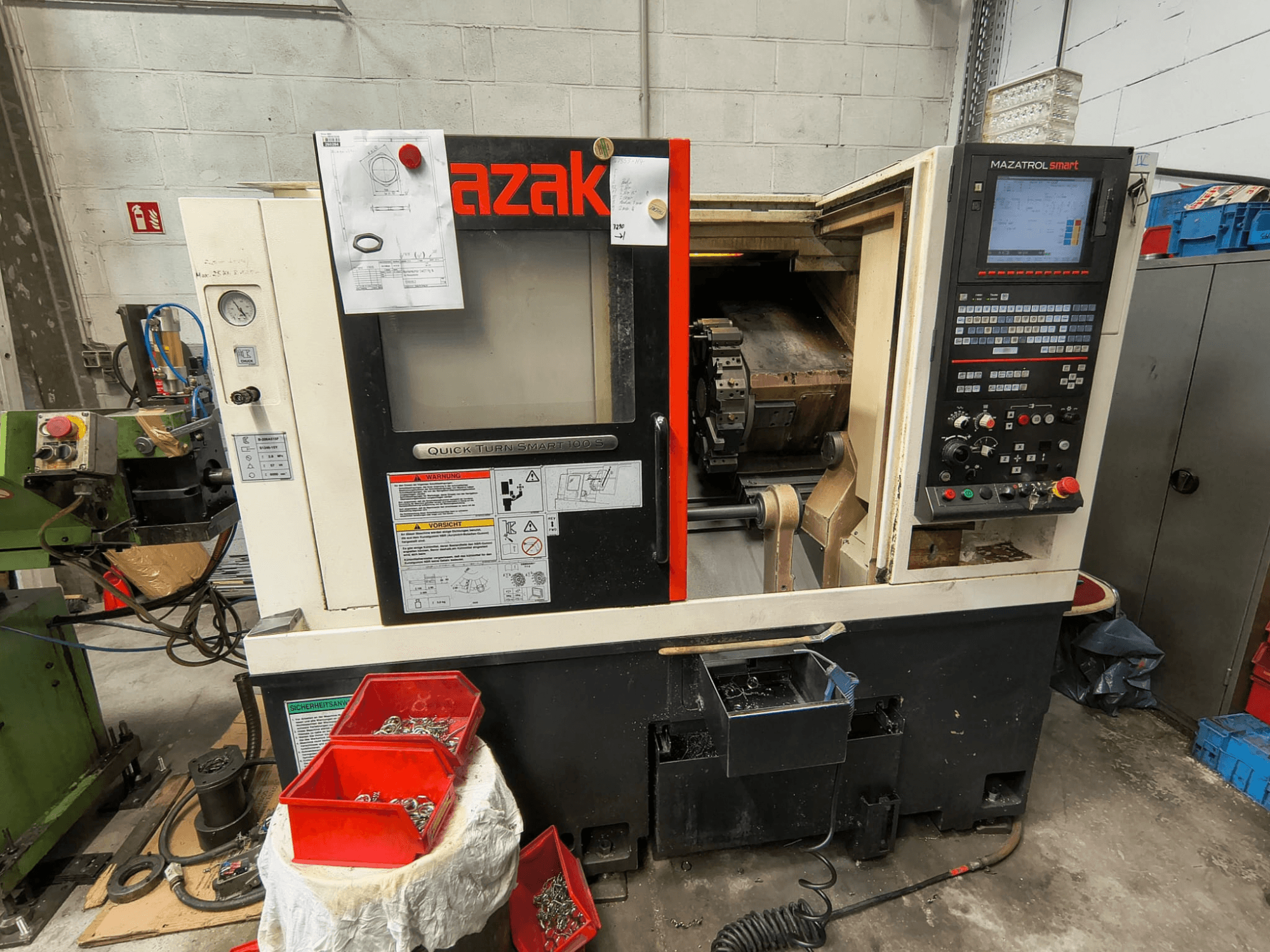 Mazak Quick Turn Smart 100 S, sidovy som visar kontrollpanelen, kylvätskebacken och förvaringsfack med skruvar.