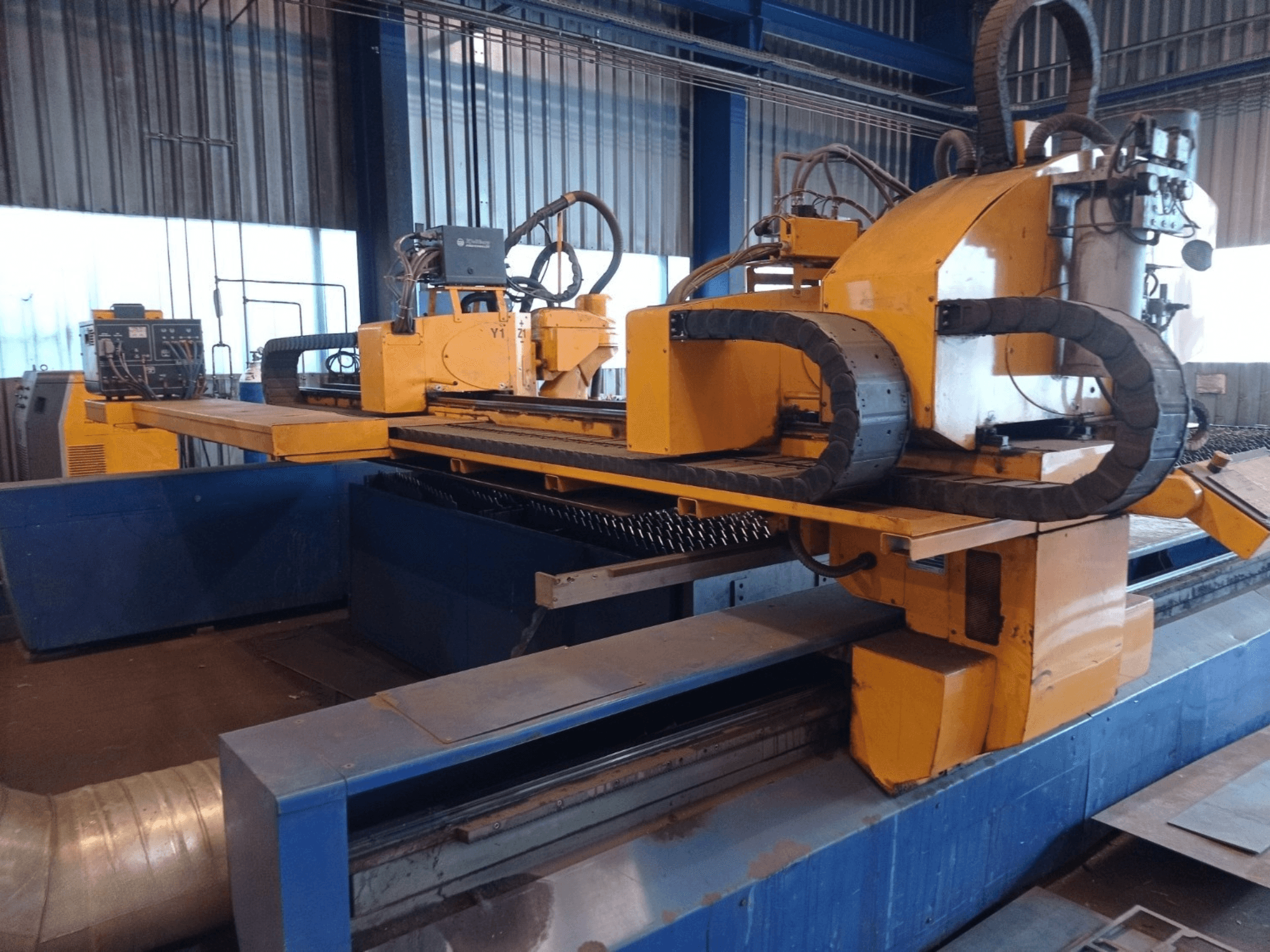 Gul CNC-plasmaskärmaskin med två horisontella armar, visad framifrån, med kontrollpanel och skärbädd.