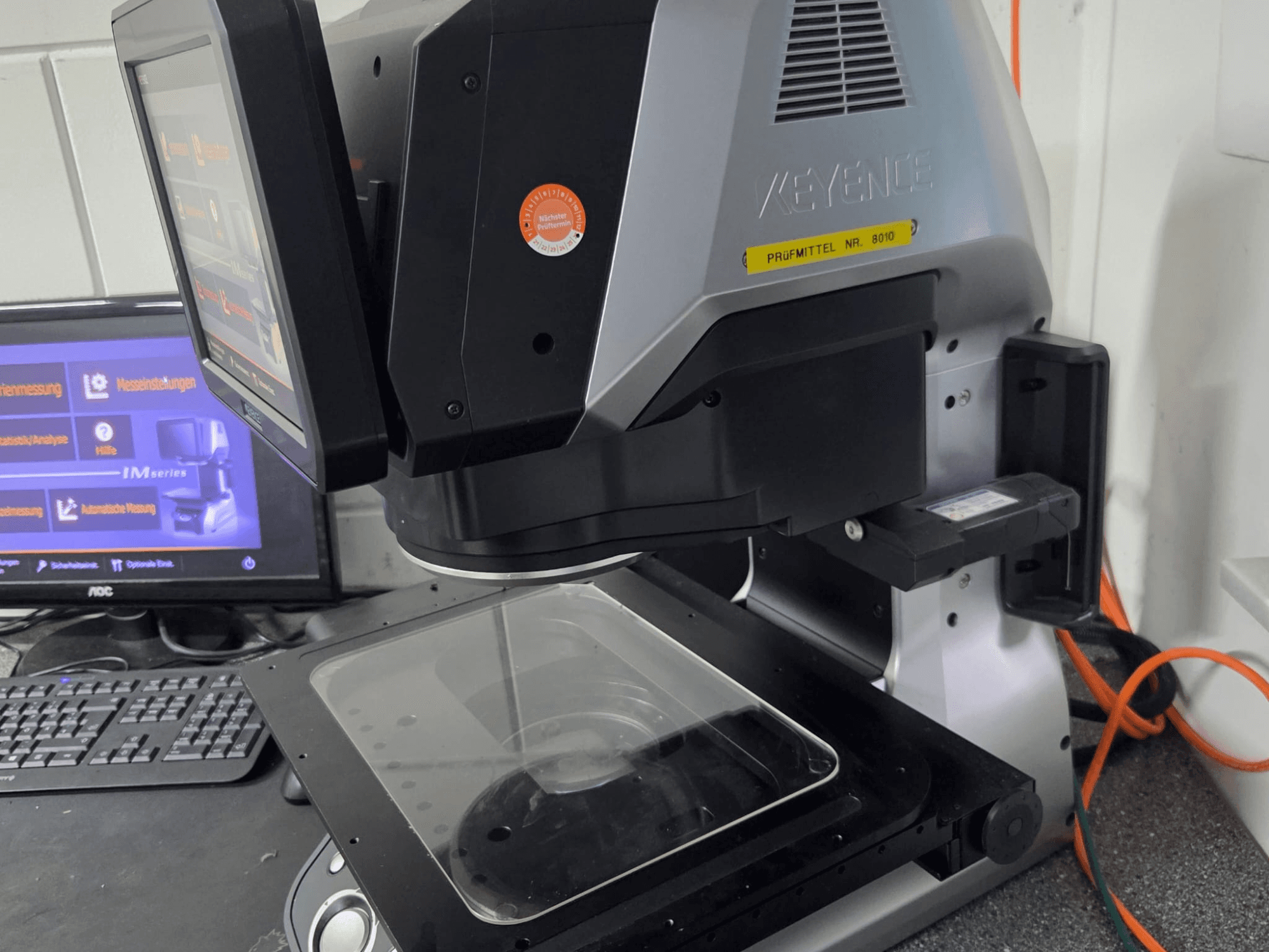 KEYENCE IM 7030 optisk mätmaskin, framifrån med pekskärm och mätplatta av glas.