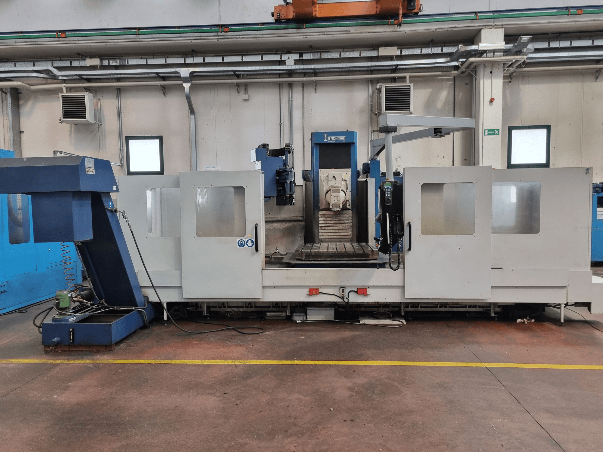 CNC-fräsmaskin av märket "Brembana", sidovy som visar kontrollpanelen och arbetsområdet med ett arbetsbord inuti.