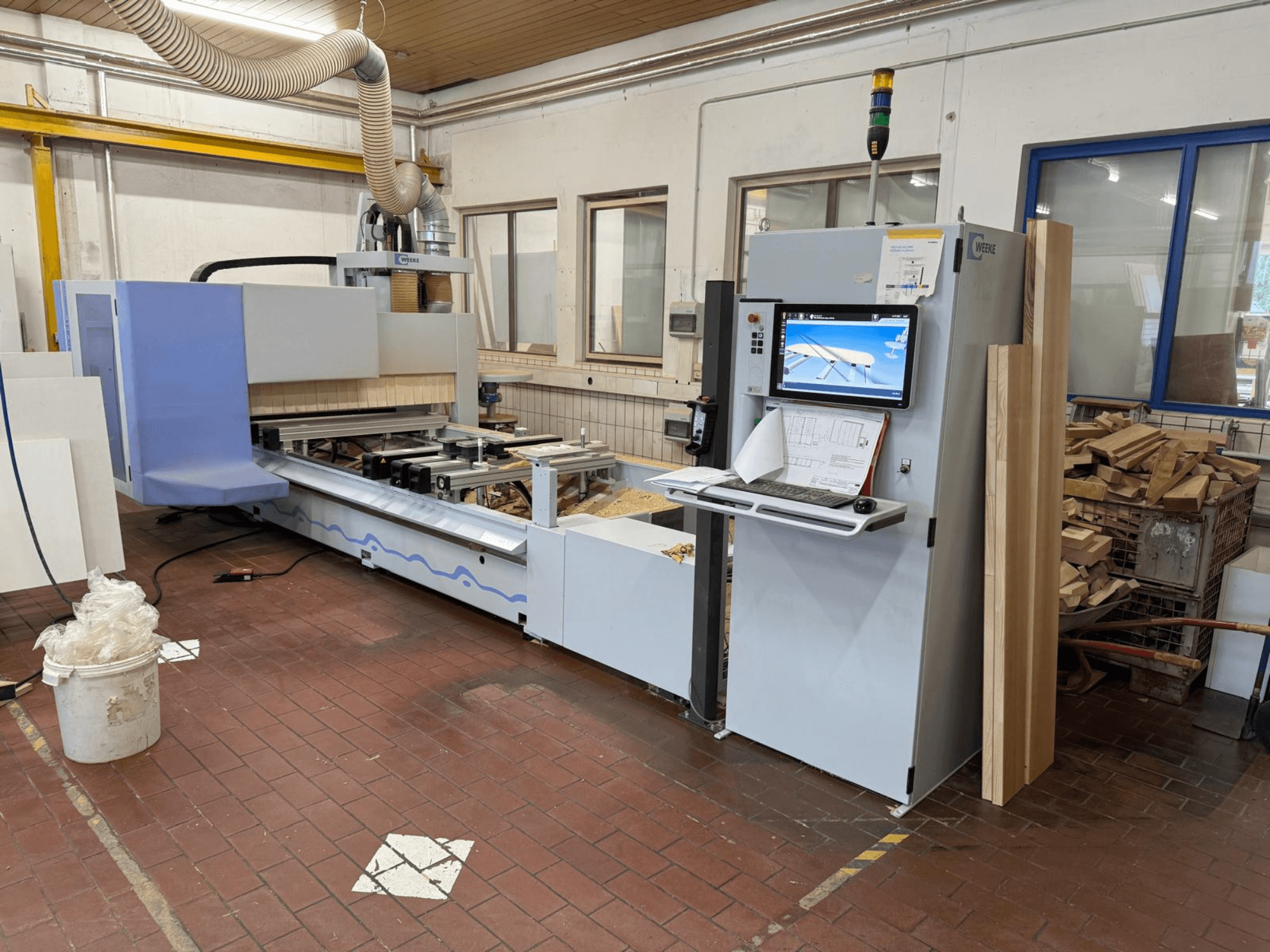 Weeke PROFI BMG211/32/12/K CNC-bearbetningscenter för trä, framifrån sett, med kontrollpanel och träbitar samt dammutsugningssystem.