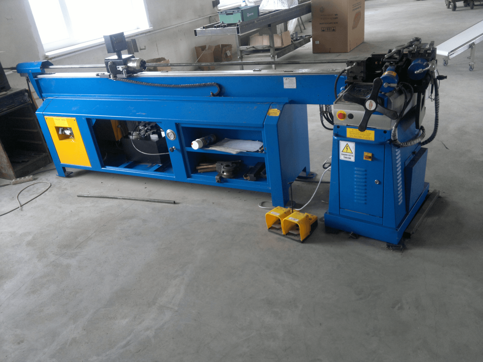 Blå träbearbetningsmaskin med gula detaljer, vy från sidan; har kontrollpanel, fotpedaler och roterande blad.