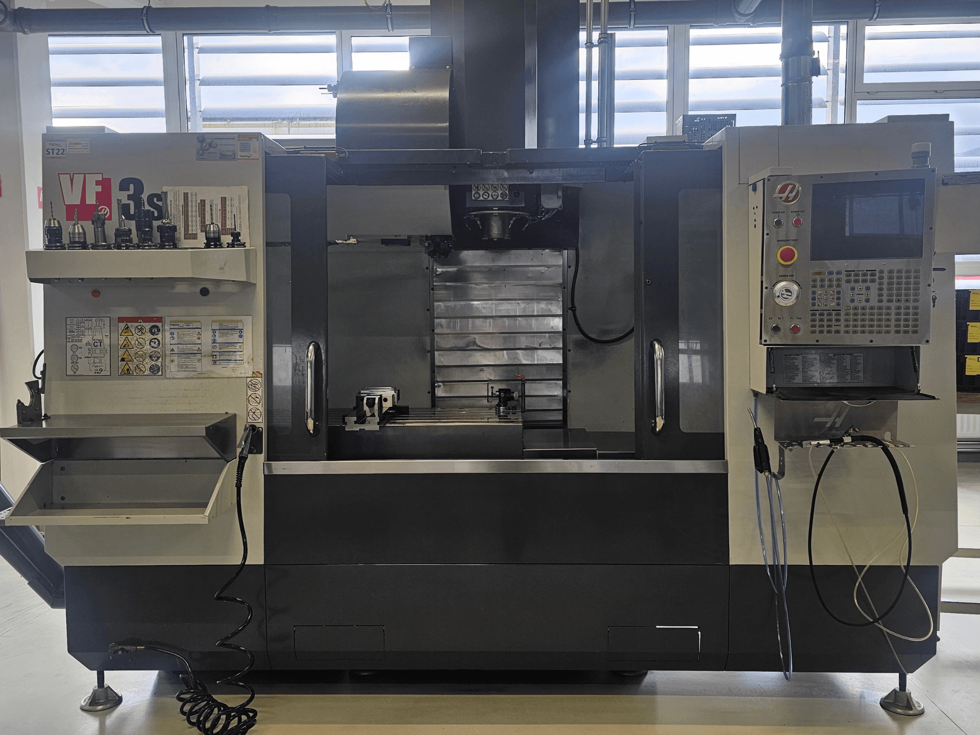 Haas VF3SS CNC-fräs, framifrån, med verktygshållare, kontrollpanel och tomt kylmedelsfack, med säkerhetsetiketter synliga.