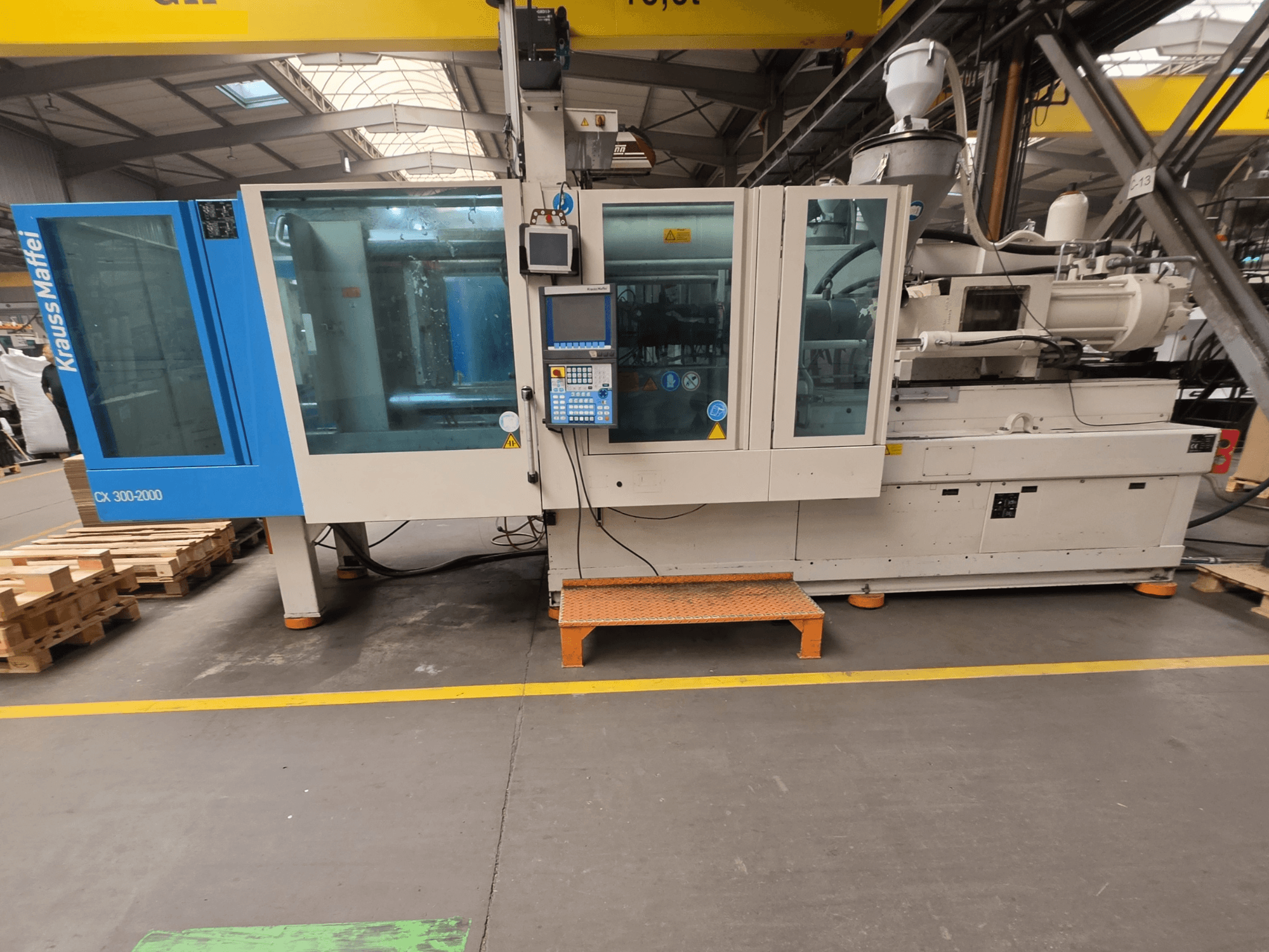 Krauss Maffei 300-2000 CX hydraulisk formsprutningsmaskin, sidovy som visar kontrollpanelen och de stora fönstren.