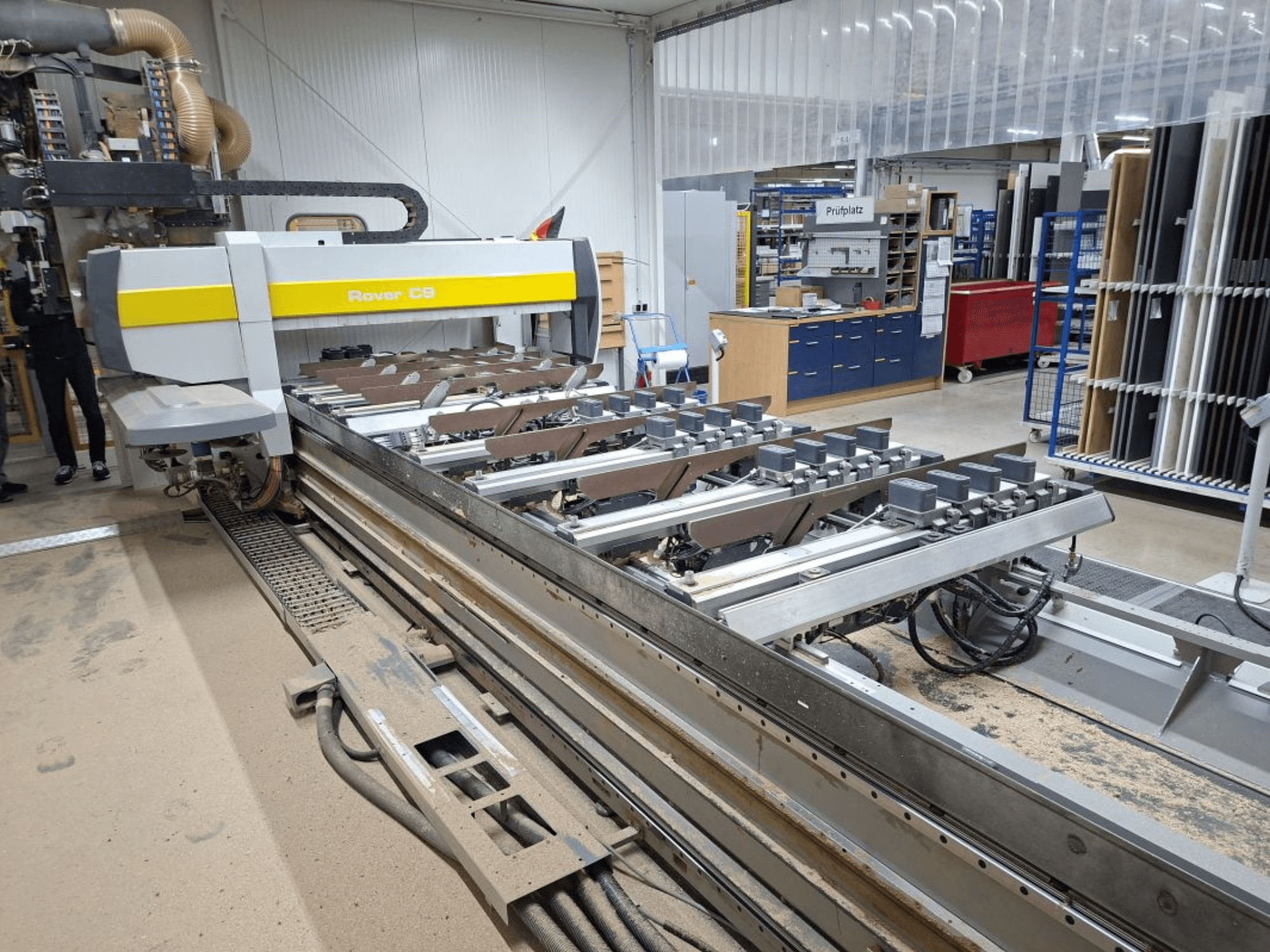 Rover C9 CNC-maskin i en verkstad; framifrån syns skärverktyg och transportörsystem med dammansamling på golvet.