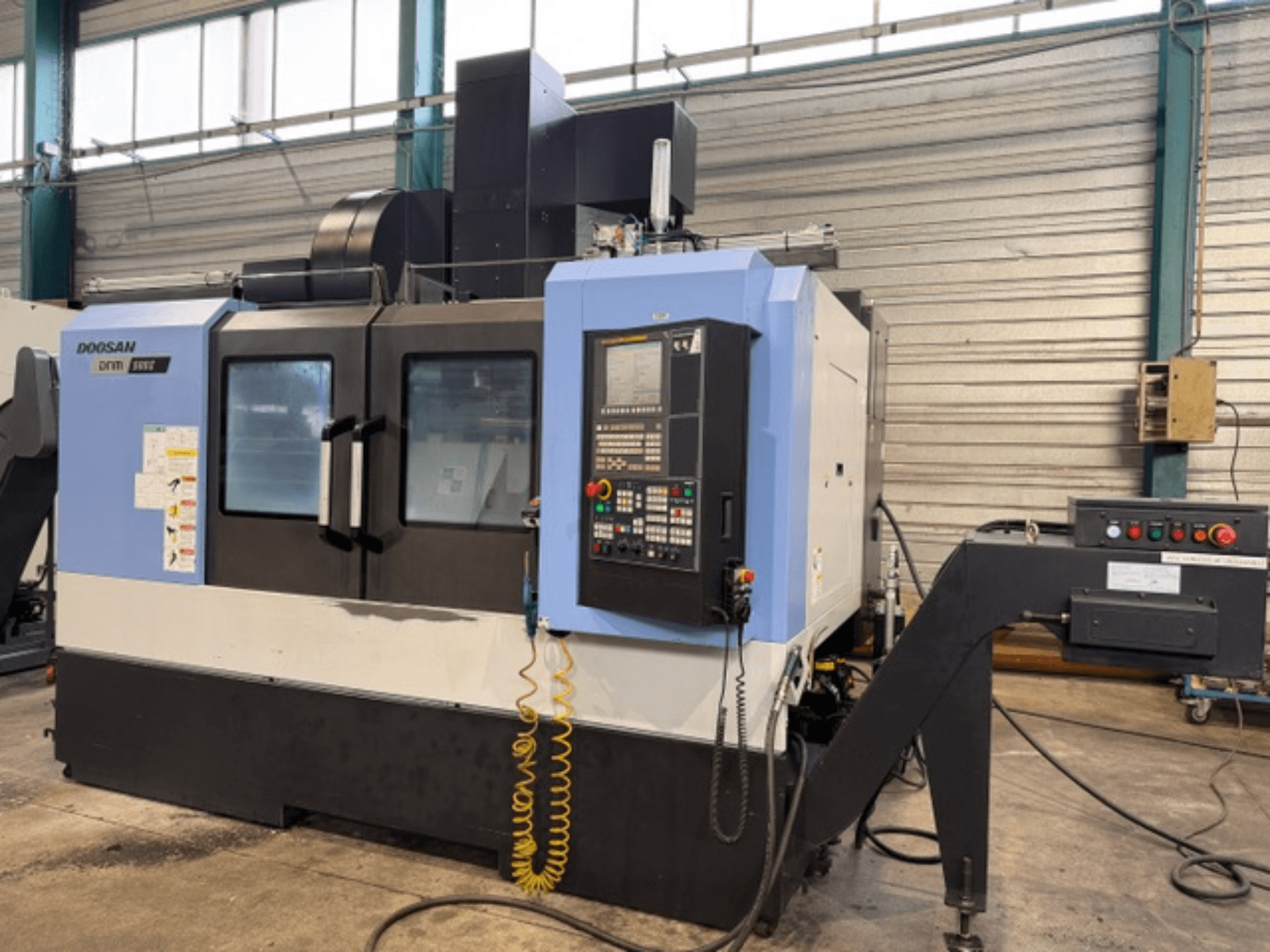 Doosan DNM 500II CNC-fräsmaskin framifrån, med kontrollpanel och verktygshållare, i fabriksmiljö.