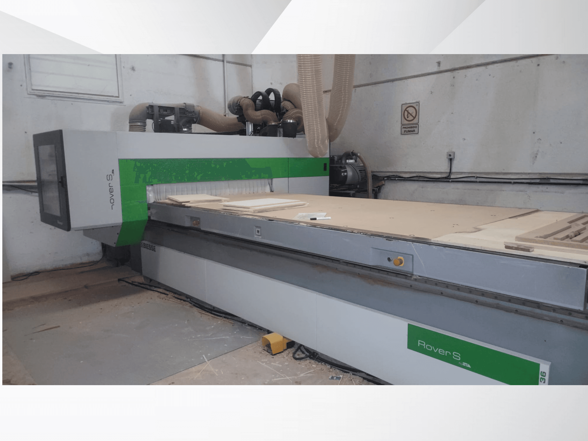 Framsidan av Biesse Rover S CNC-maskin, med stor arbetsyta med träpaneler och slangar för dammutsugning.