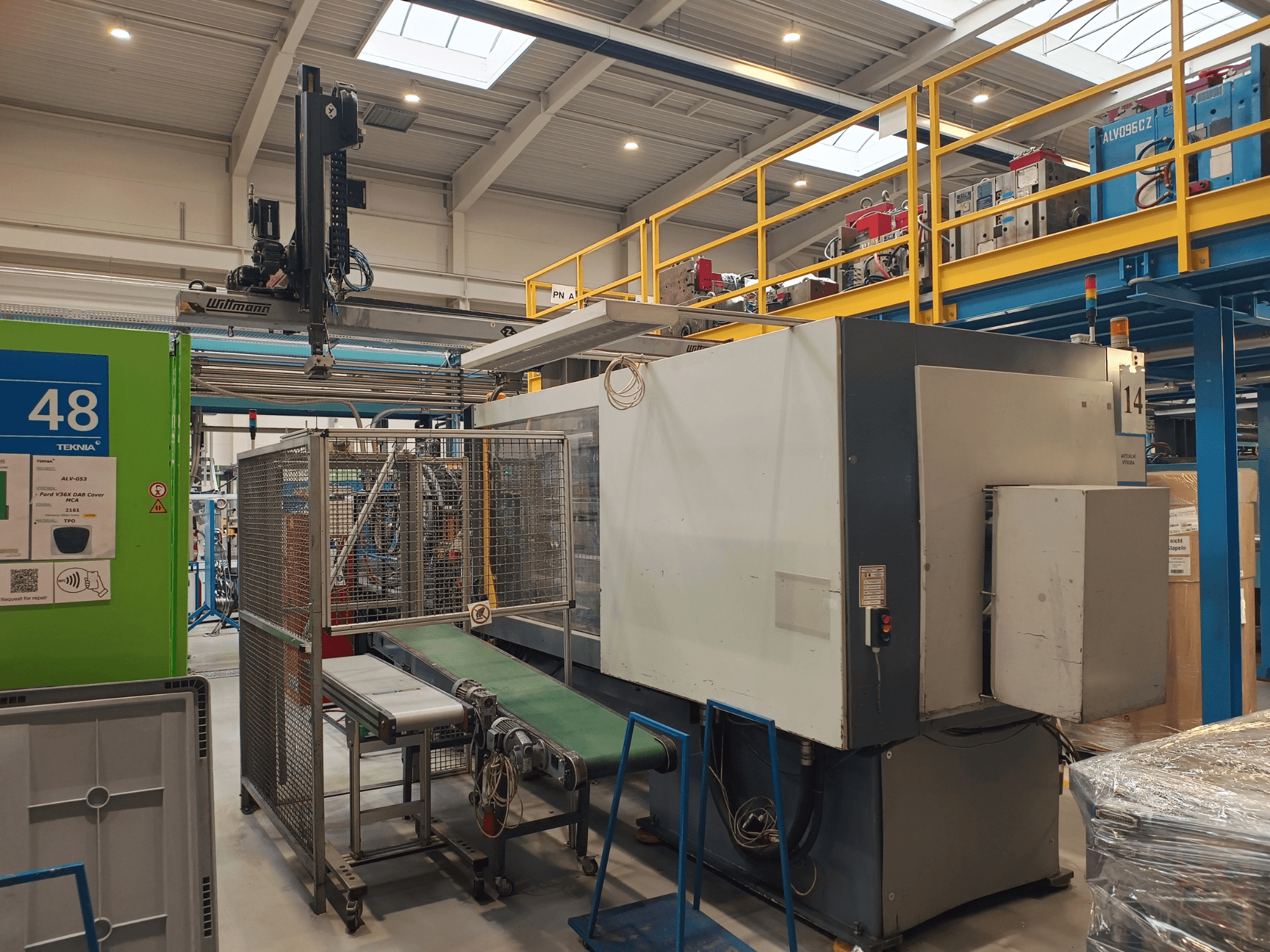 Industriell automationsmaskin från Winmon, sidovy som visar transportband, kontrollpanel och säkerhetsbur i en fabriksmiljö.