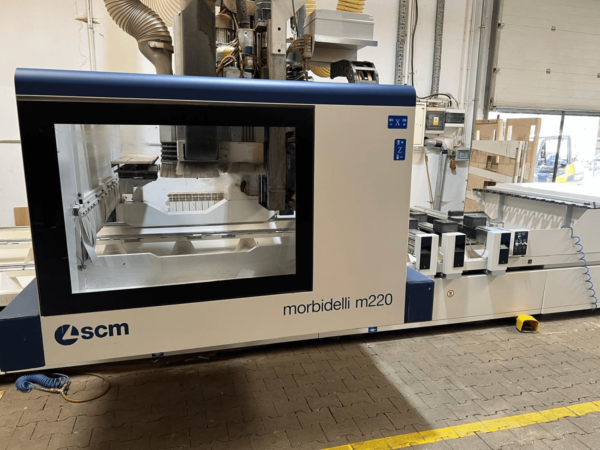 Framifrånvy av CNC-bearbetningscentret SCM Morbidelli M220, där det stora fönstret, kontrollpanelen och arbetsområdet syns.