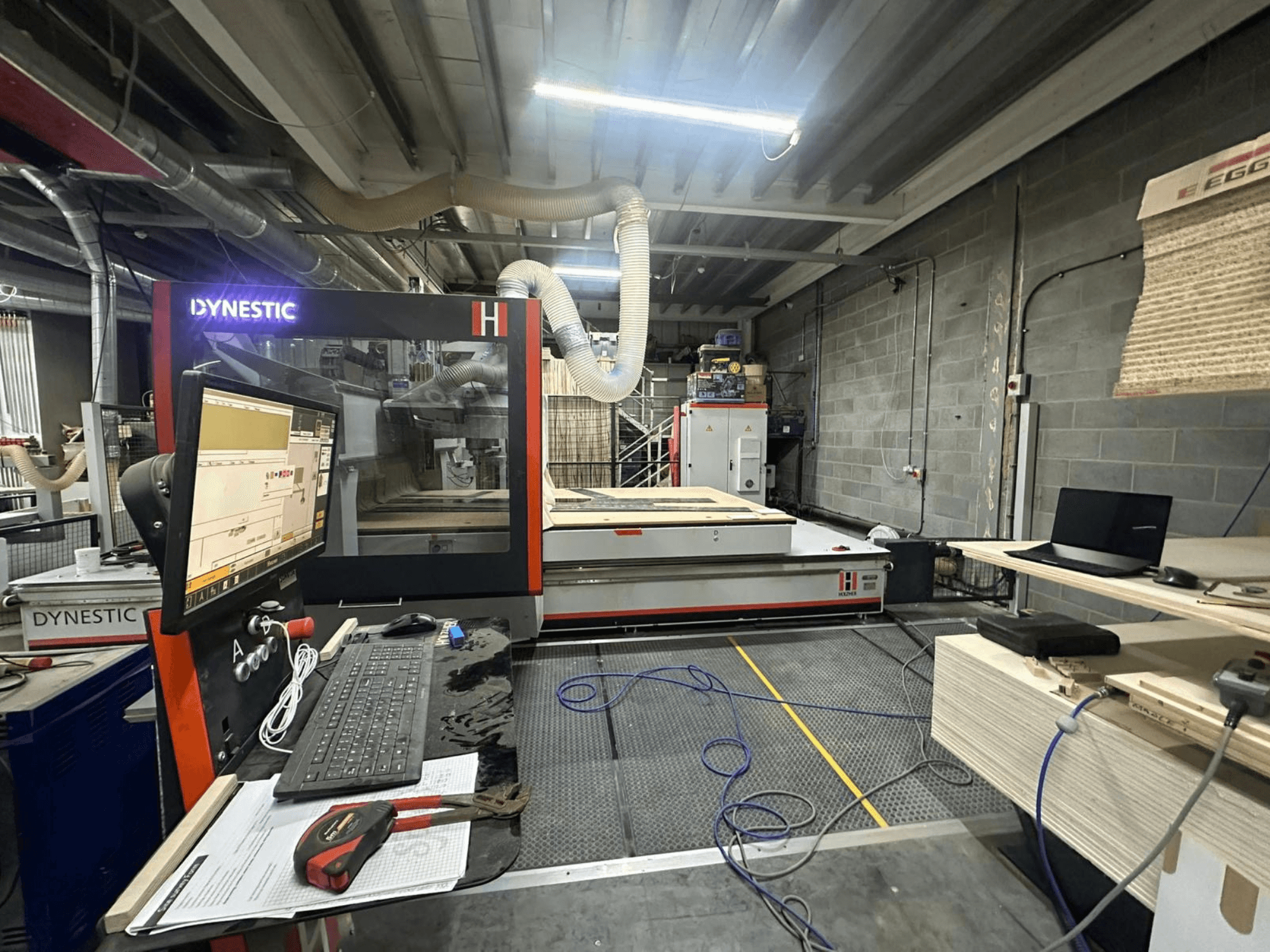 HOLZHER Dynestic 7535 träkvarn i verkstad, visar kontrollpanel, monitor och material på arbetsbordet, framifrån.