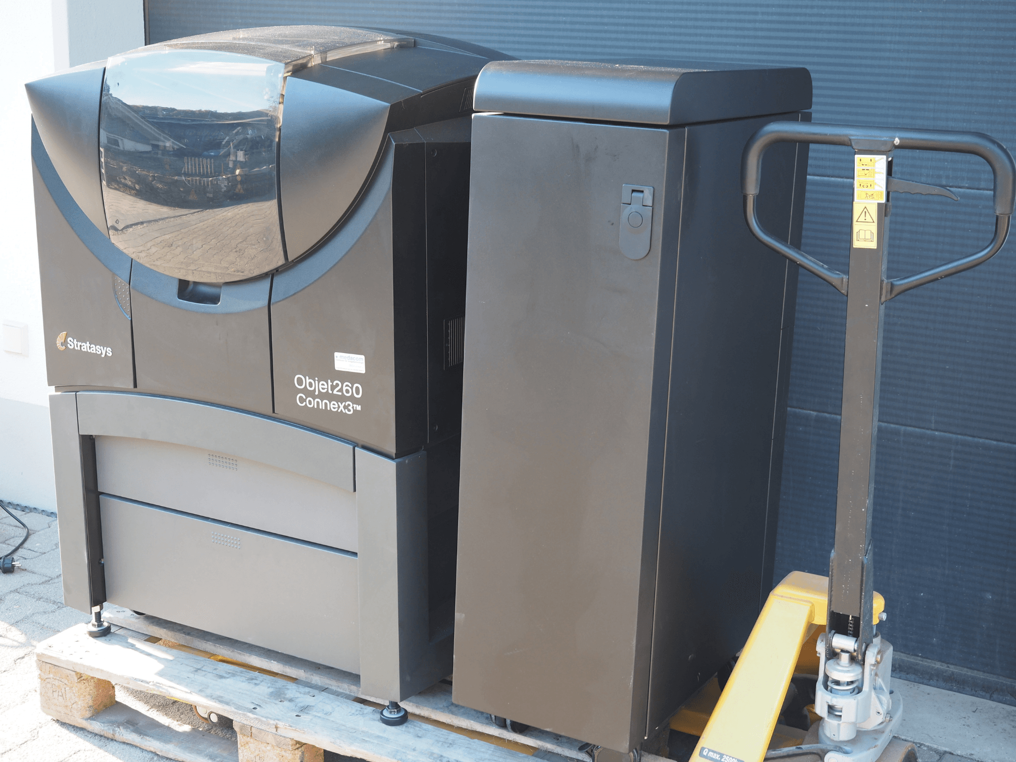Stratasys Objet260 Connex3 3D-skrivare för plast, sidovy, har kompakt design med kontrollpanel och ansluten materialbehållare.