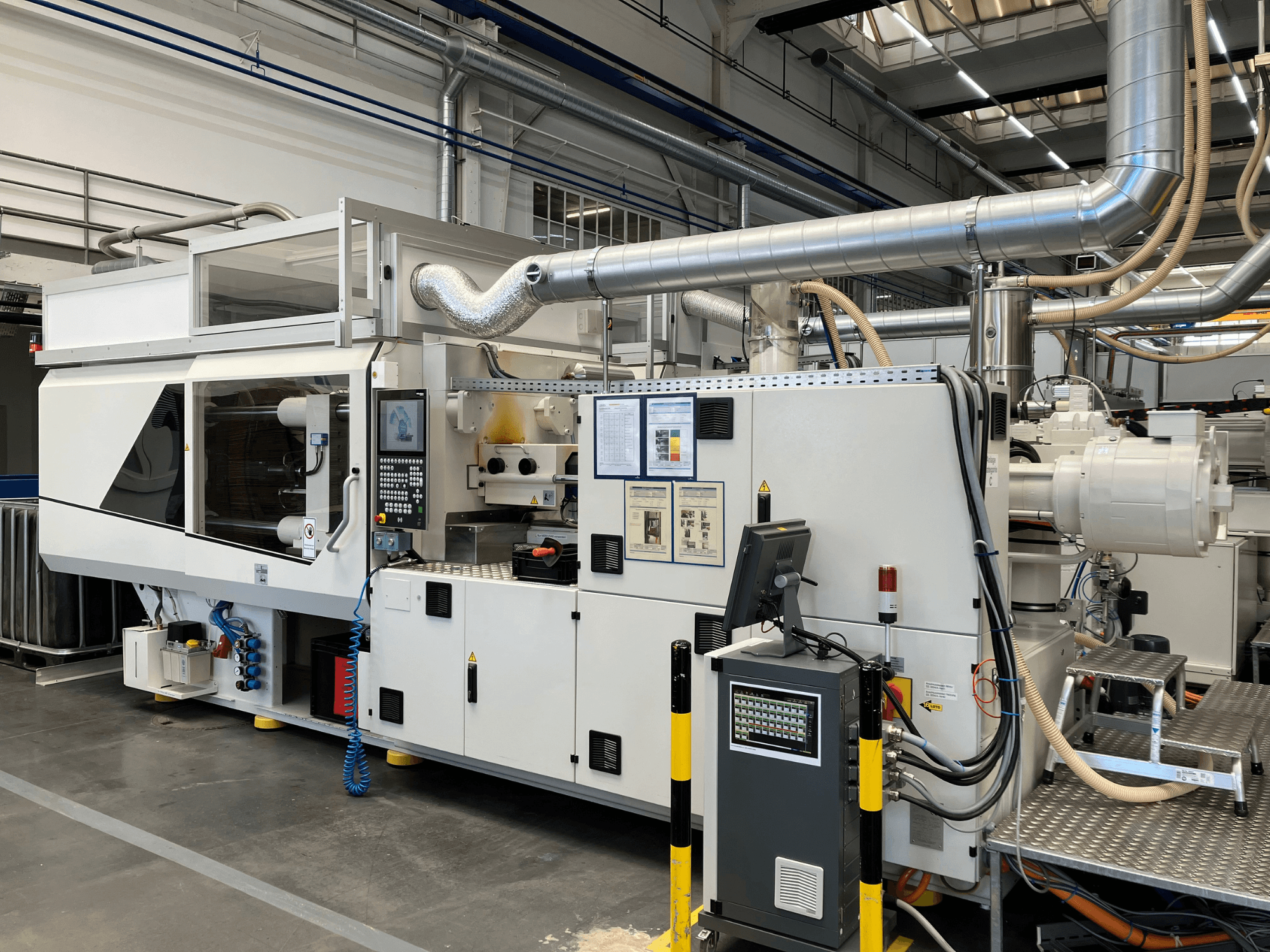 Frontvy av en industrimaskin med kontrollpanel, rör och displayskärmar, med en elegant vit design och tekniska detaljer.