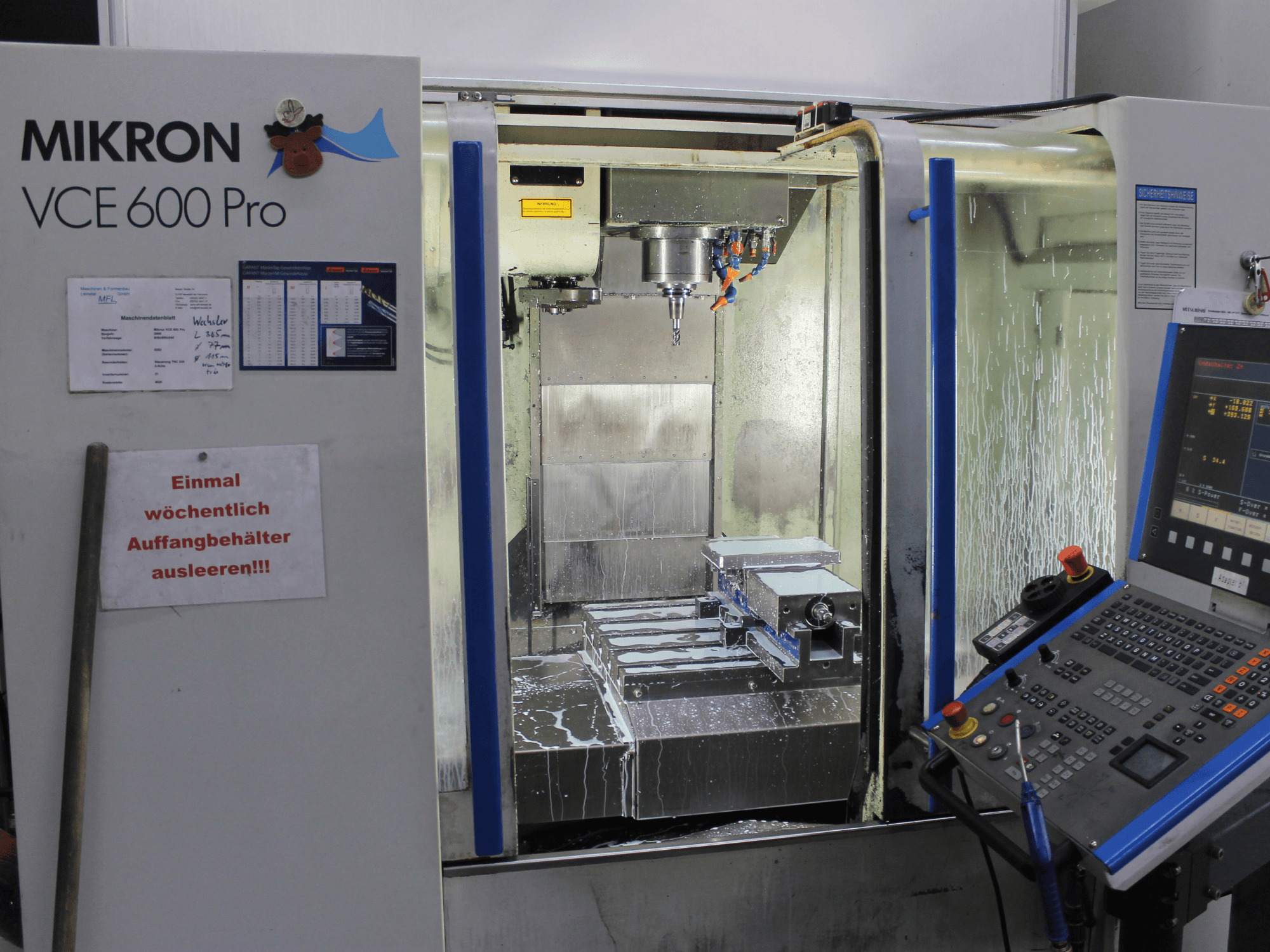 Mikron VCE 600 Pro bearbetningscenter, framifrån, med skärverktyg, kylvätskespray och kontrollpanel med knappar.
