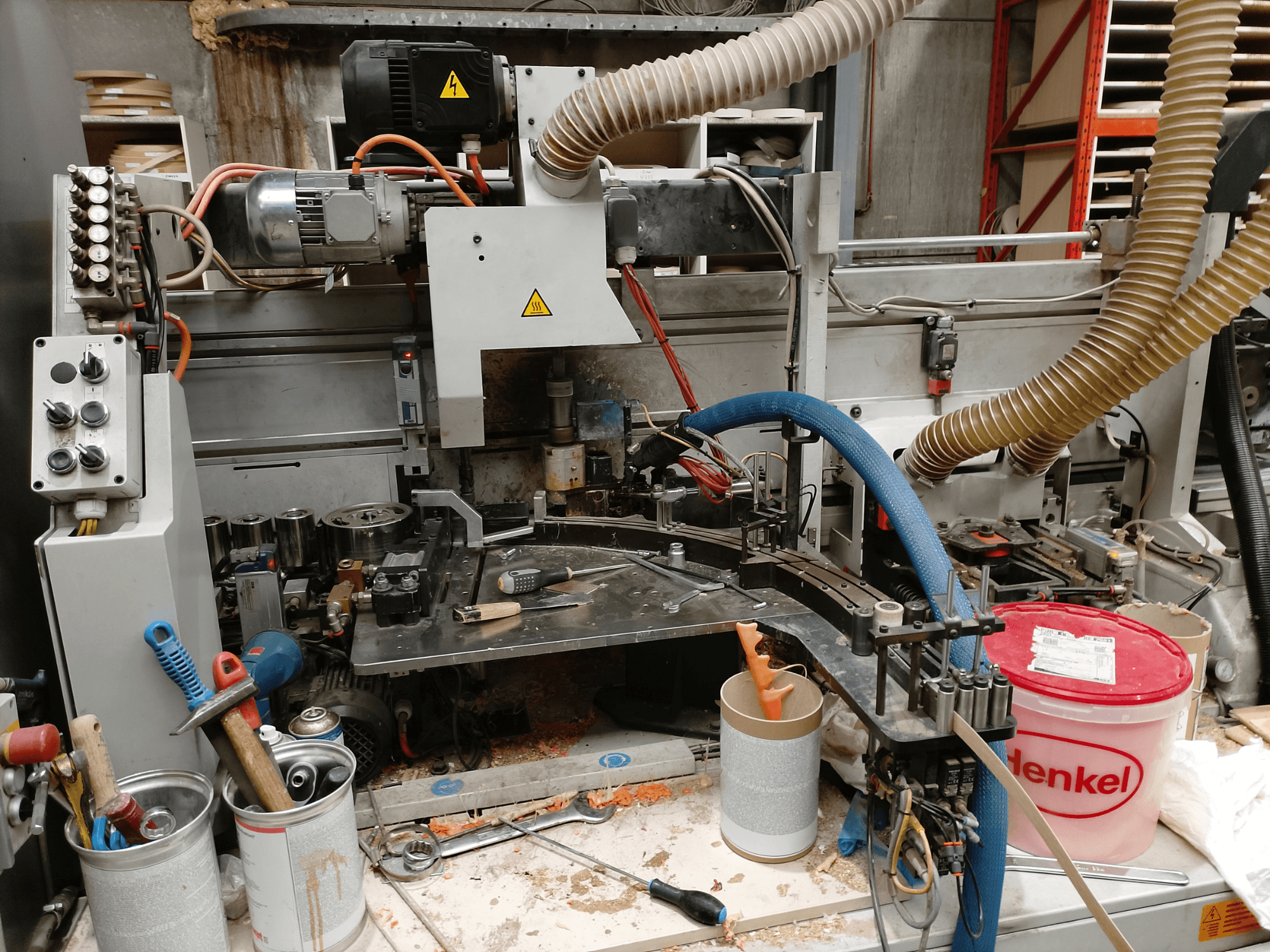 BIESSE Edge Stram B1 kantlistmaskin i frontvy, där maskiner, slangar och arbetsverktyg syns bland träspån.