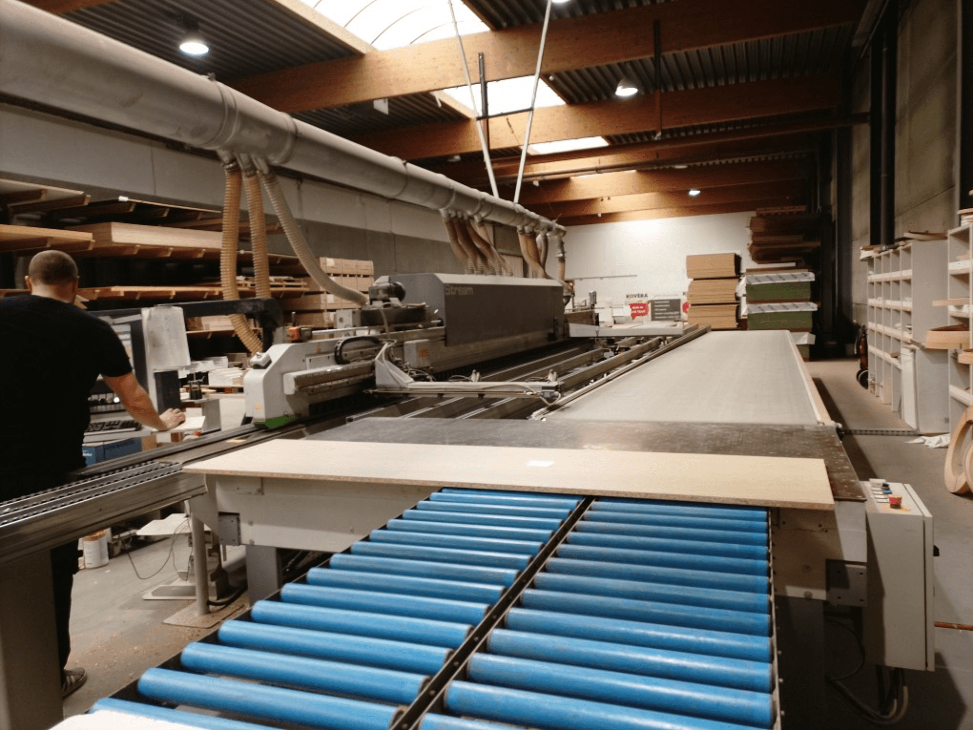 BIESSE Edge Stream B1 kantlistmaskin, sidovy som visar operatör, blå rullar och träskiva på transportör.