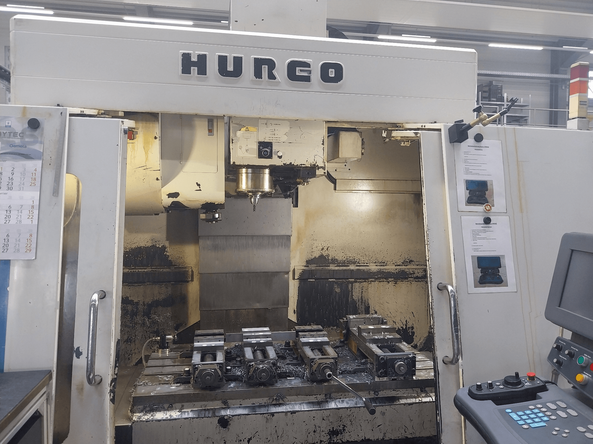 Hurco VMX 42 vertikal bearbetningscenter framifrån, visar arbetsbord med fixturer och kontrollpanel, något slitet skick.