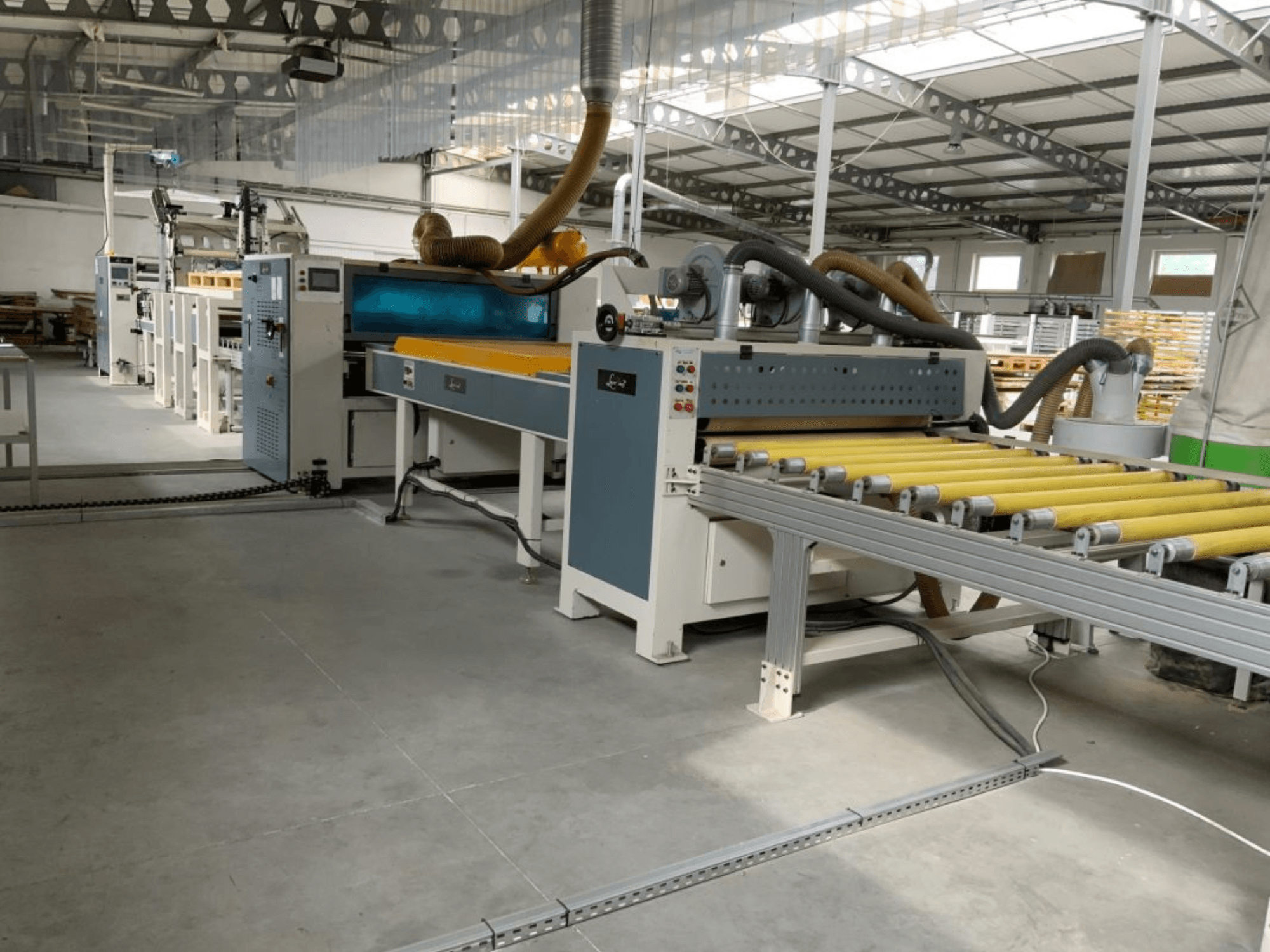Lamineringspressen MASTER PUR-1400 i en fabriksmiljö, sett framifrån, med rullar och manöverreglage i bild.