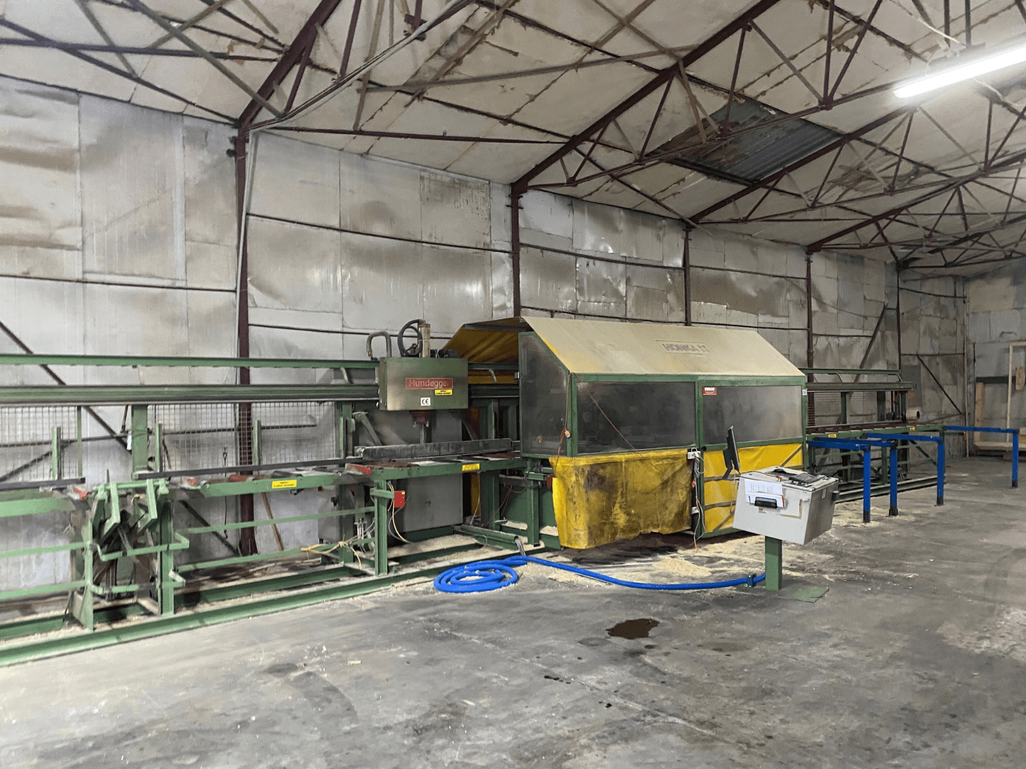 CNC-bearbetningscenter för trä HUNDEGGER K1 i en verkstad, sidovy som visar maskiner, reglage och sågspån på golvet.