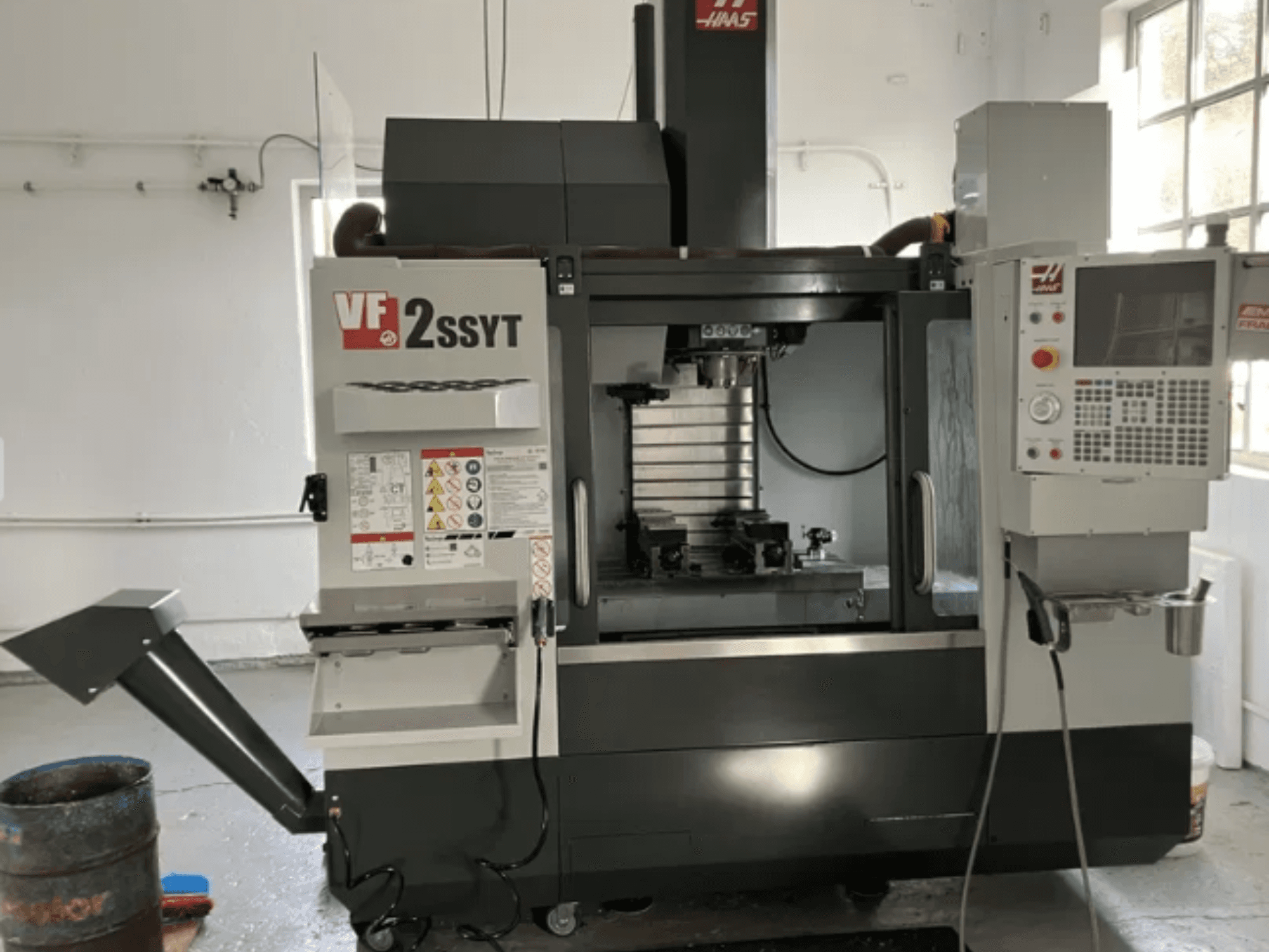 Haas VF-2SSYT CNC-fräs, framifrån, har kontrollpanel, verktygshållare och kylvätskesystem för metallbearbetning.