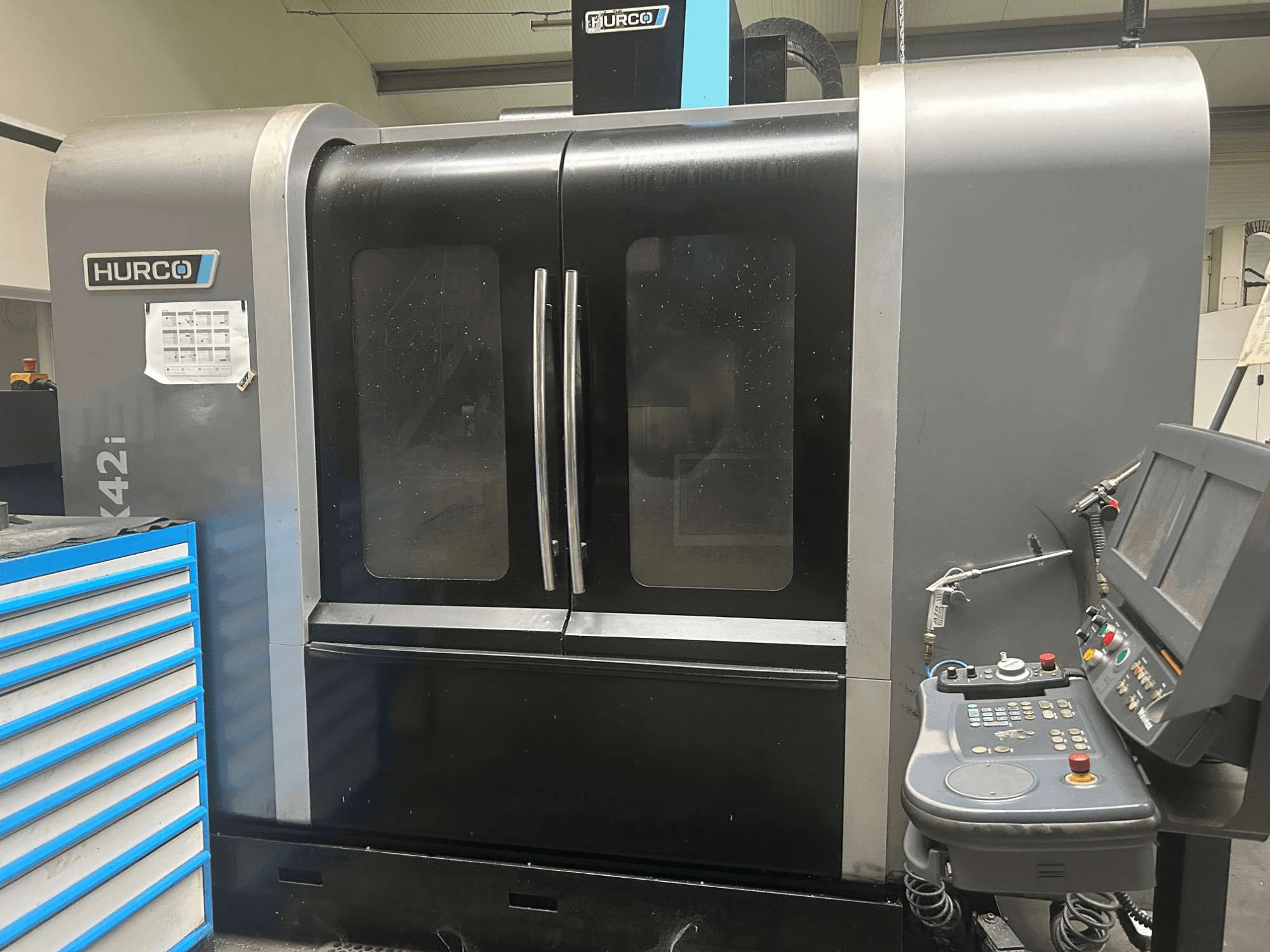Hurco VMX42i CNC-maskin, framifrån med kontrollpanelen på sidan, har dubbla dörrar och synliga tekniska detaljer.