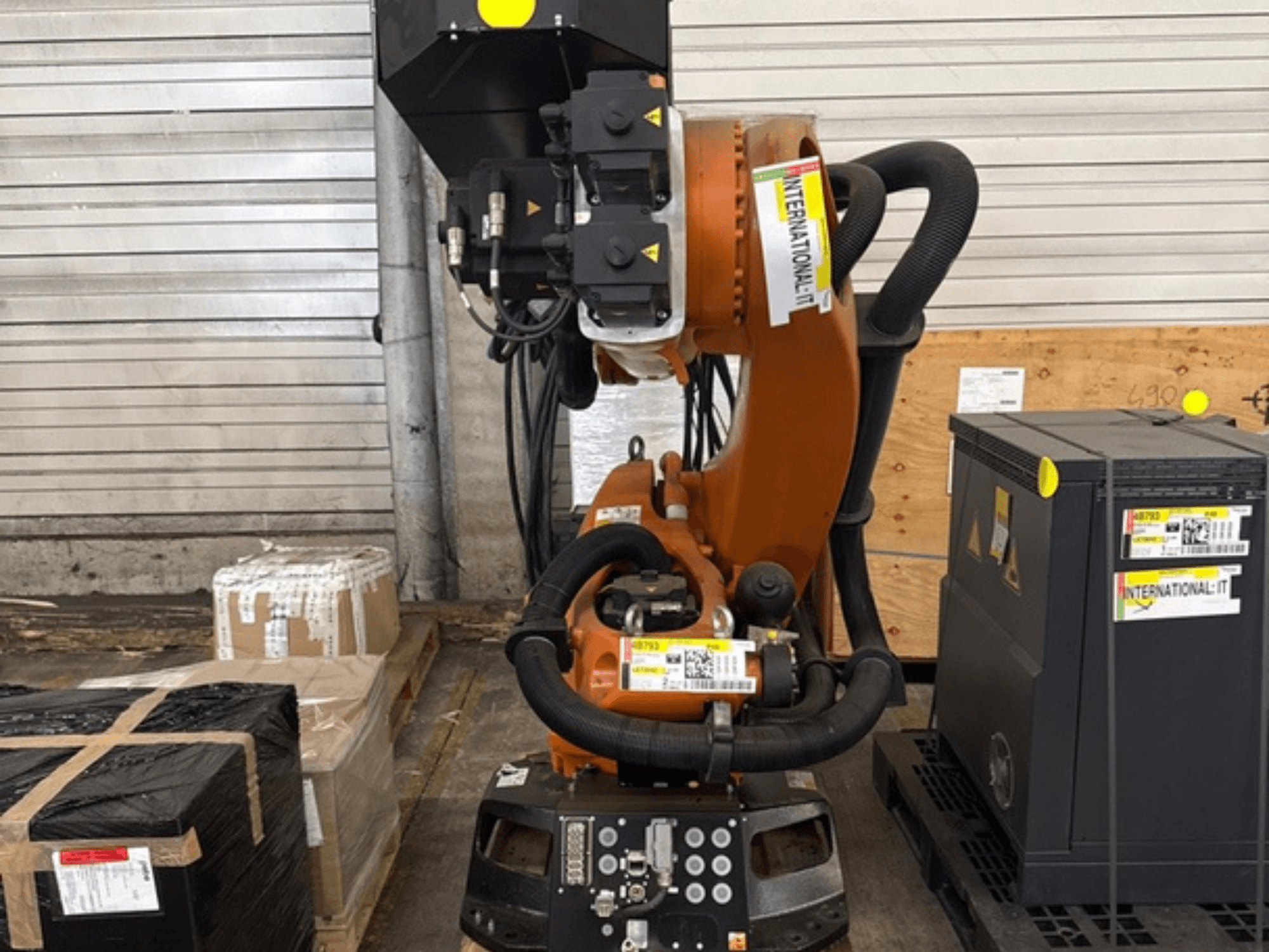 KUKA KR 210 R2700 – en extra robotarm sedd framifrån, placerad på en pall bredvid förpackningar och utrustning.
