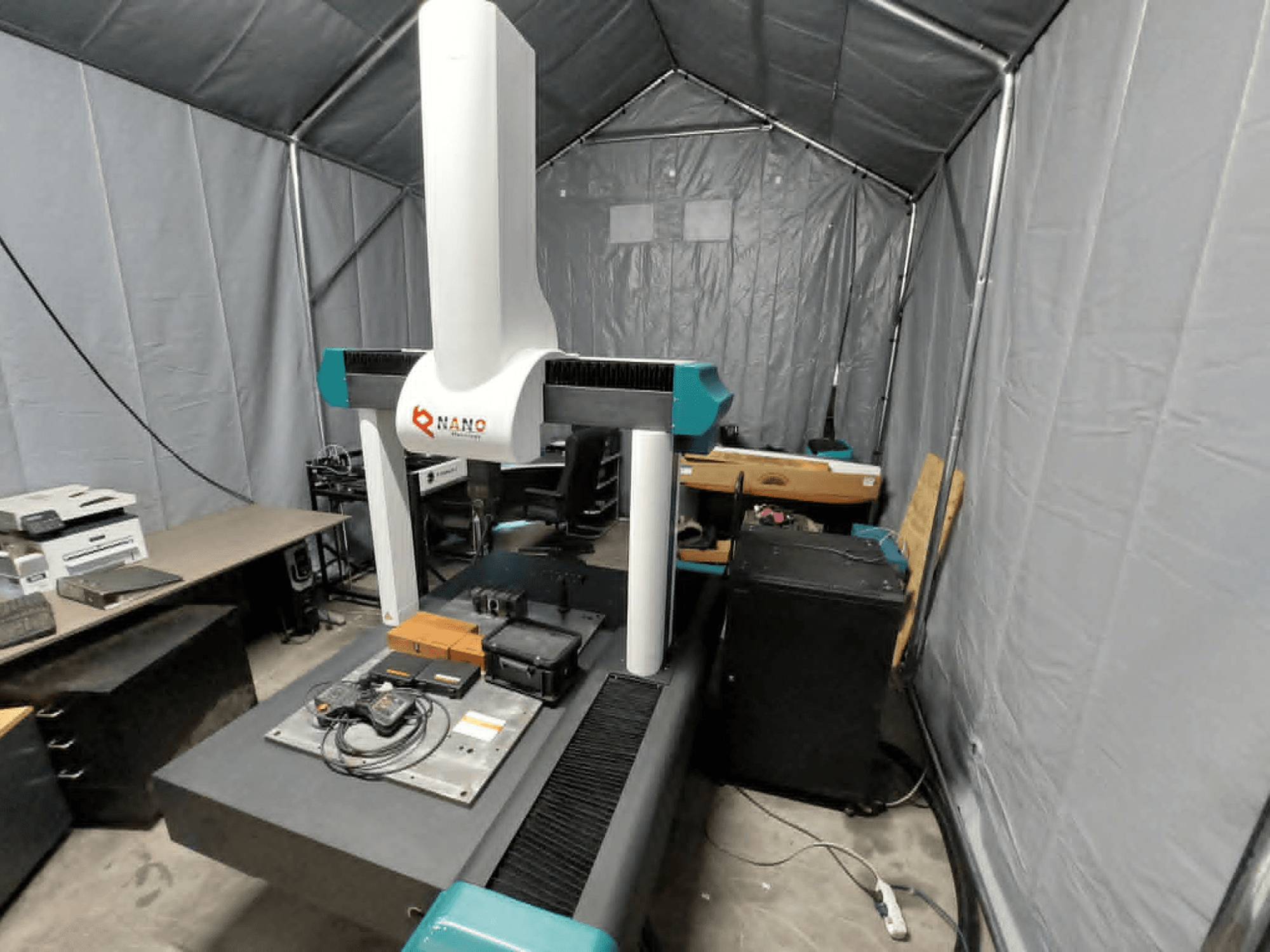 NANO METROLOGY Micr 7106 CMM i ett tält; framifrån syns maskinens arm och mätplattform med tillbehör.